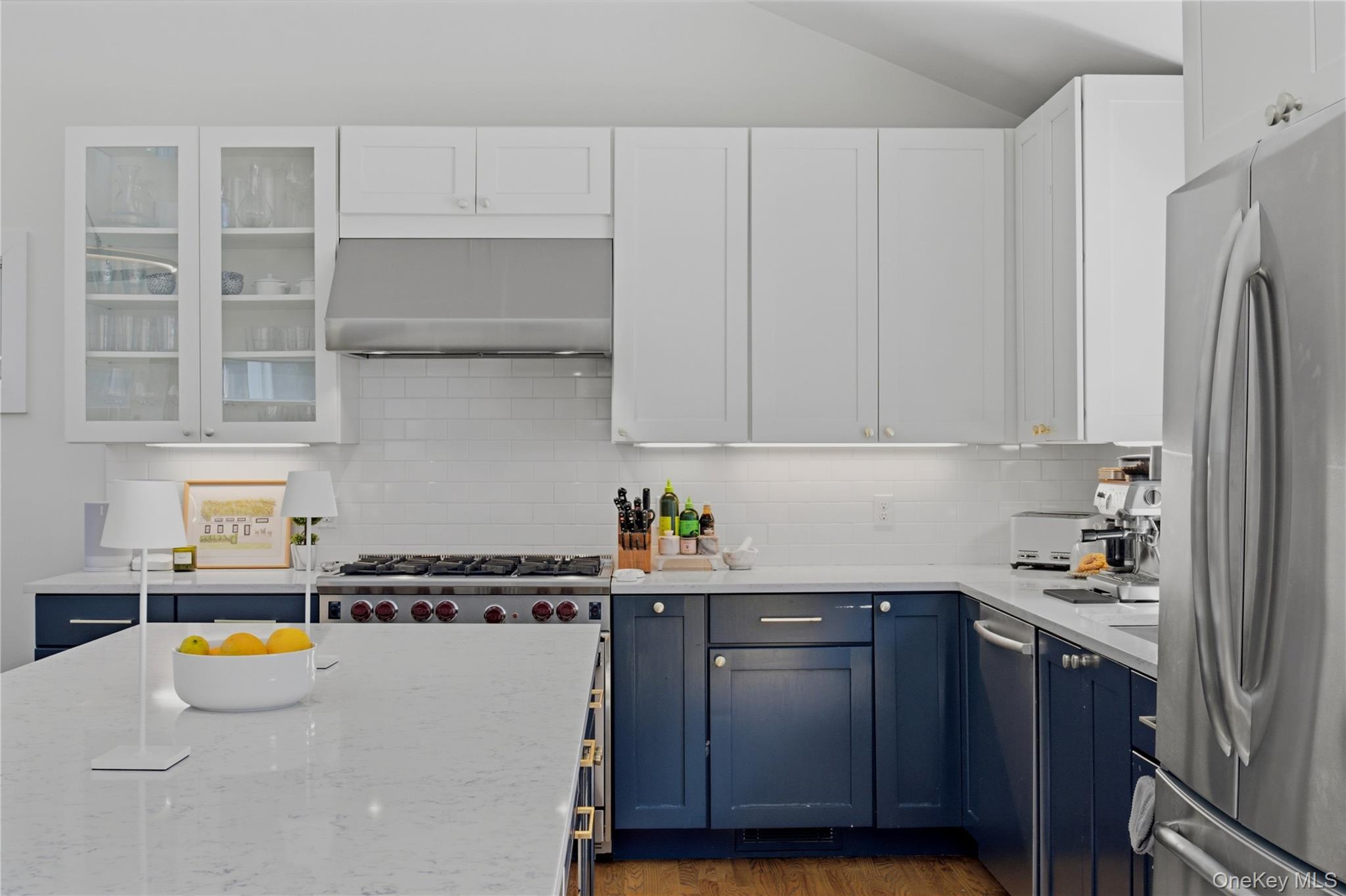 Kitchen with navy lower cabinets, white island, stainless appliances, and a wide gas range.