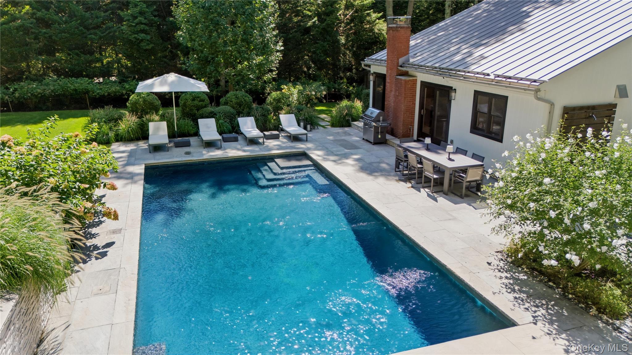 Swimming pool beside a stone patio with lounge chairs and outdoor dining area.