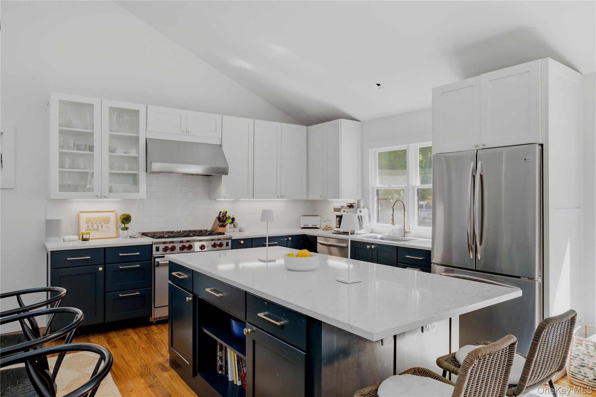 Kitchen with a large white island, navy cabinets, stainless steel appliances, and a gas range.