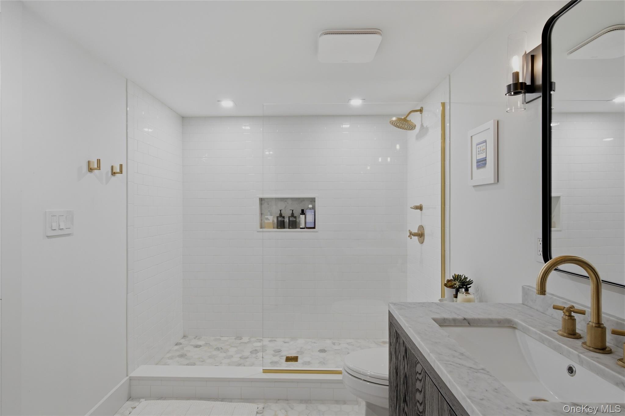 Bathroom with a glass walk-in shower, marble floor, and dark vanity with brass fixtures.