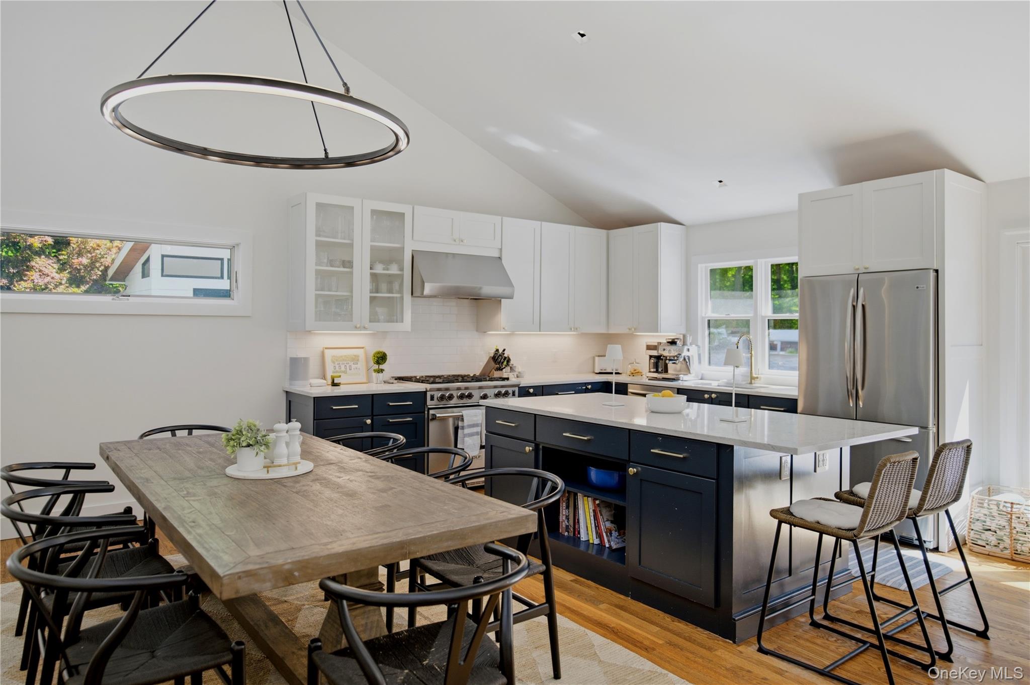 Kitchen with navy cabinets, a large island, stainless appliances, and a rustic dining table.