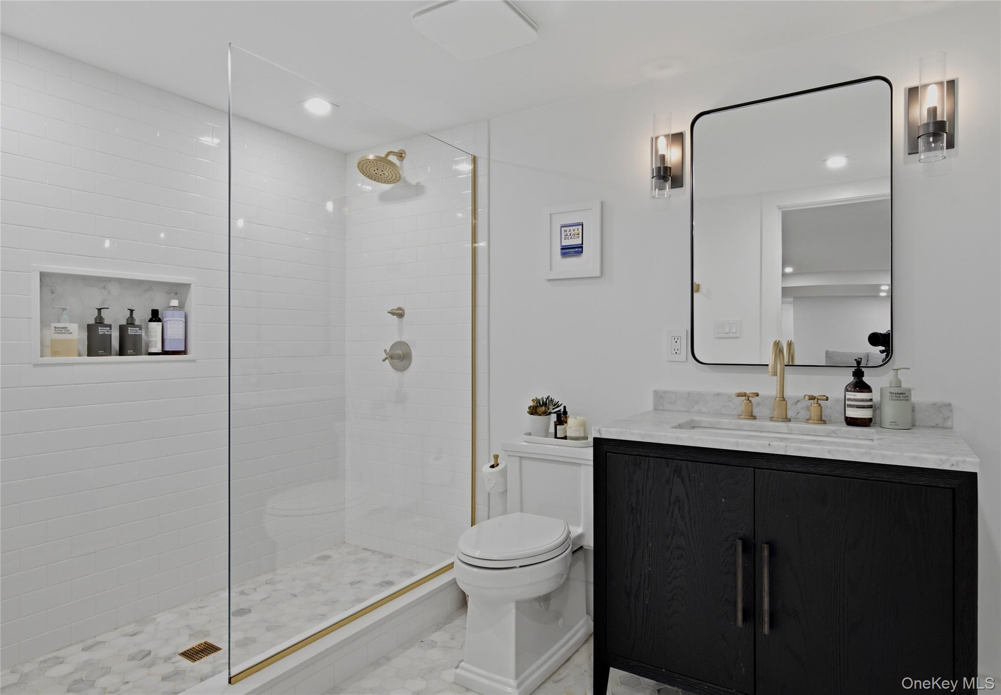 Bathroom with a glass shower, brass fixtures, and a dark wood vanity topped with marble.