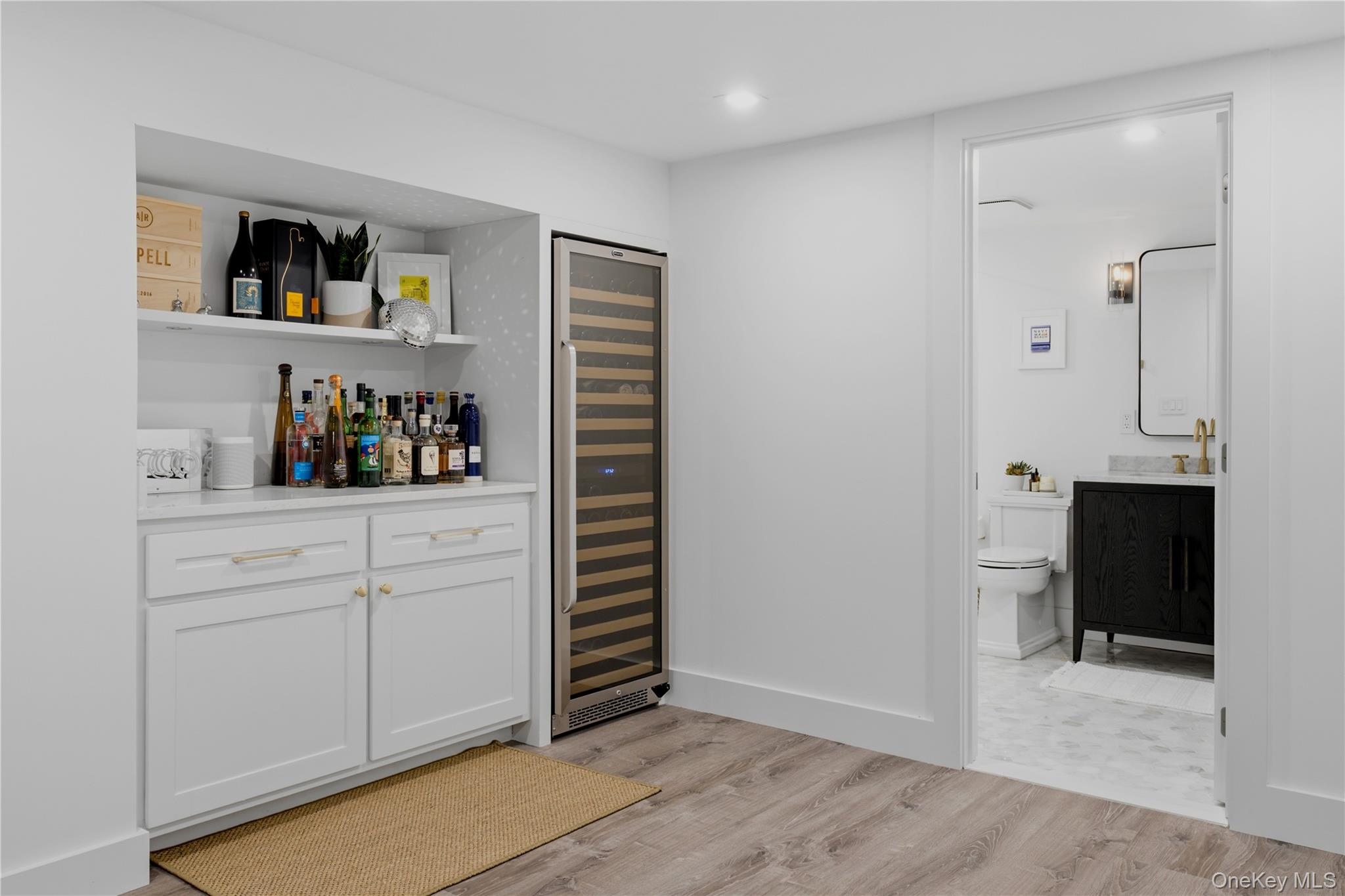 Built-in wet bar with a glass-front wine refrigerator beside an open doorway to a bathroom.