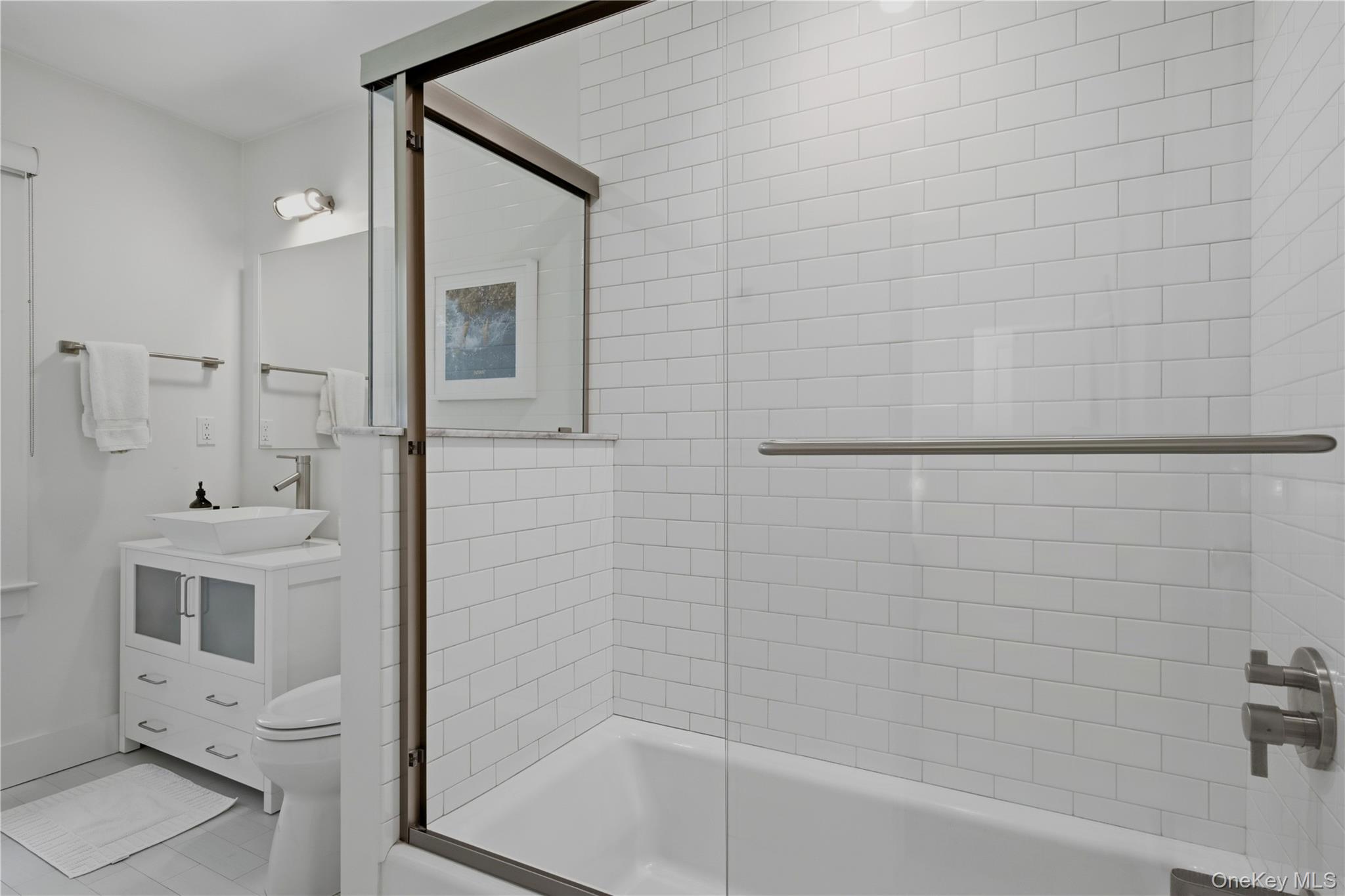 Bathroom with a glass-enclosed tub, white subway tile, grab bar, and vessel sink vanity.