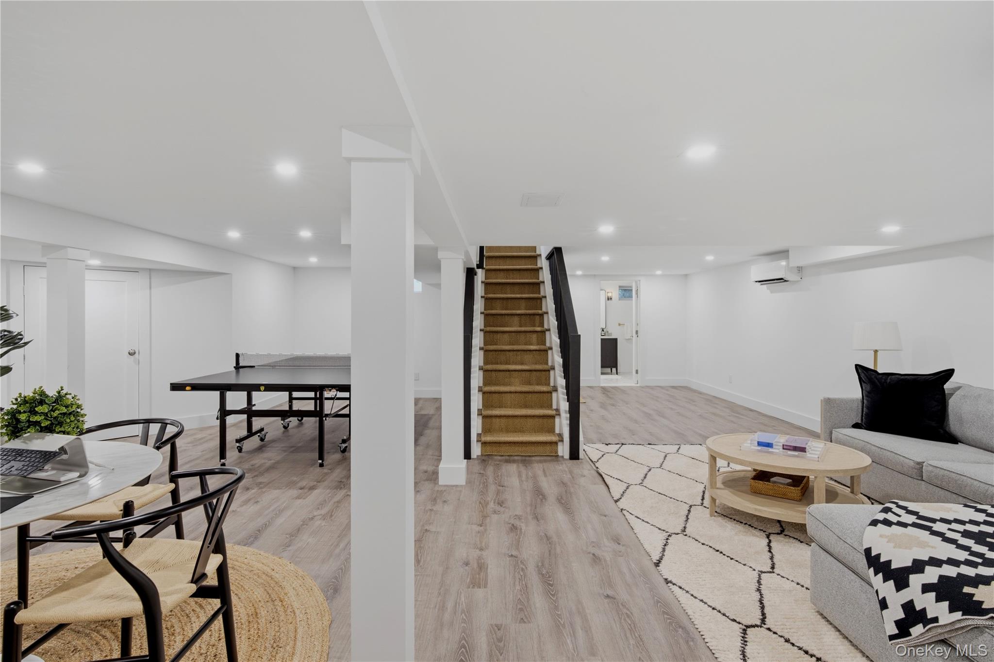 Finished lower-level recreation room with a central staircase, ping-pong table, and staged seating area.