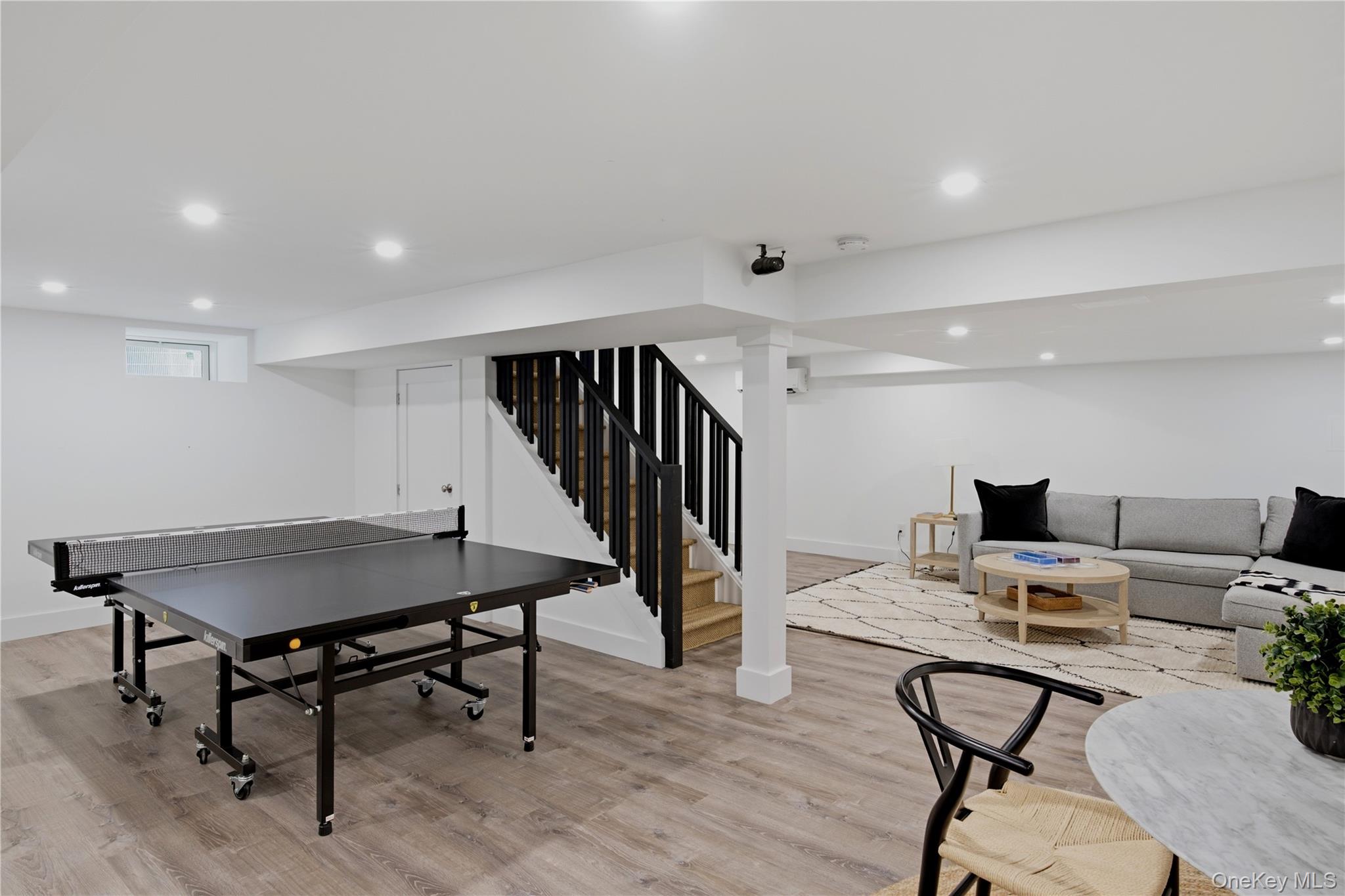 Basement recreation room with a table tennis table, black-railed staircase, and gray sectional sofa.