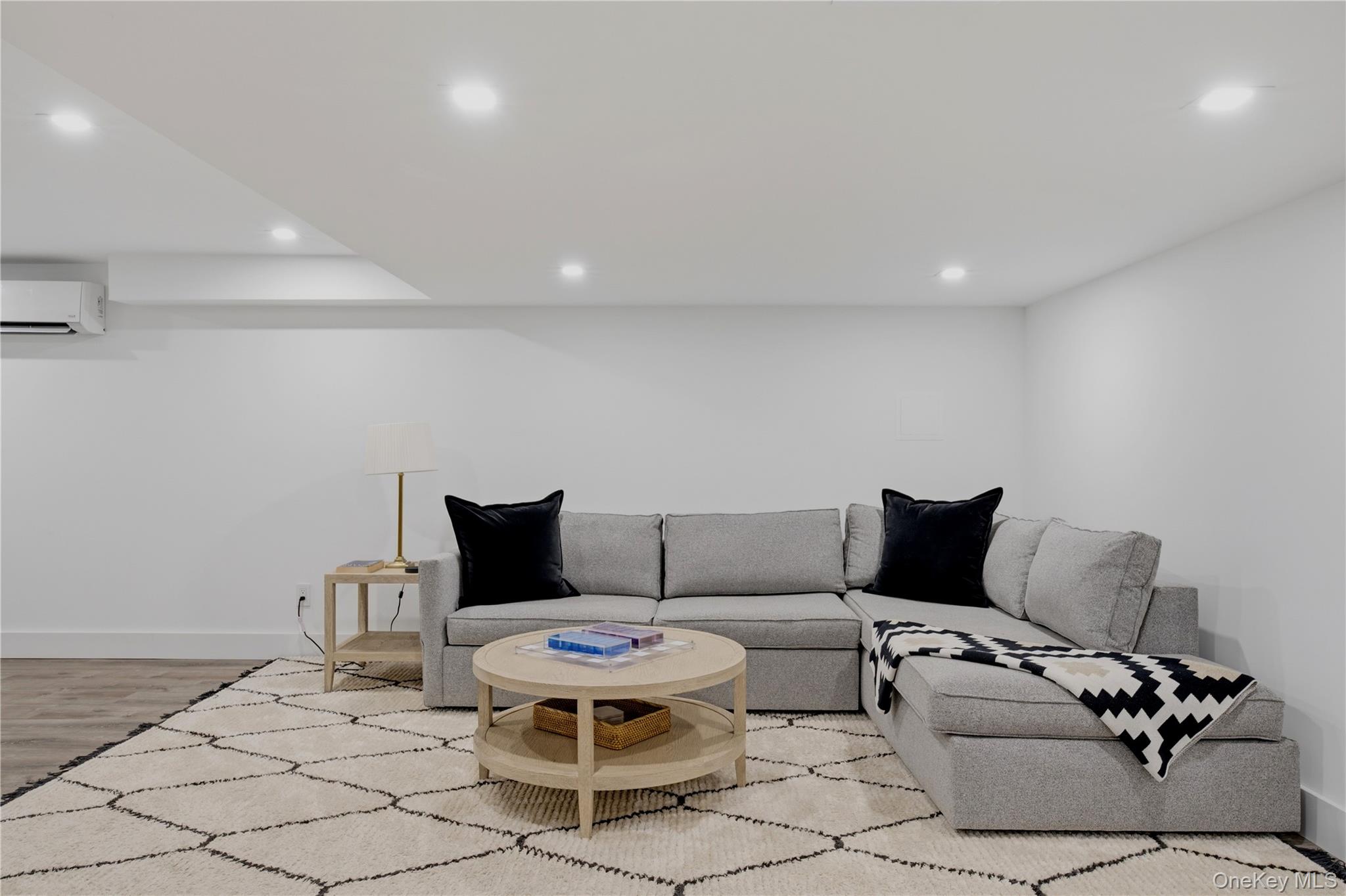 Living room with a gray sectional, round wood coffee table, and cream rug with black diamond pattern.
