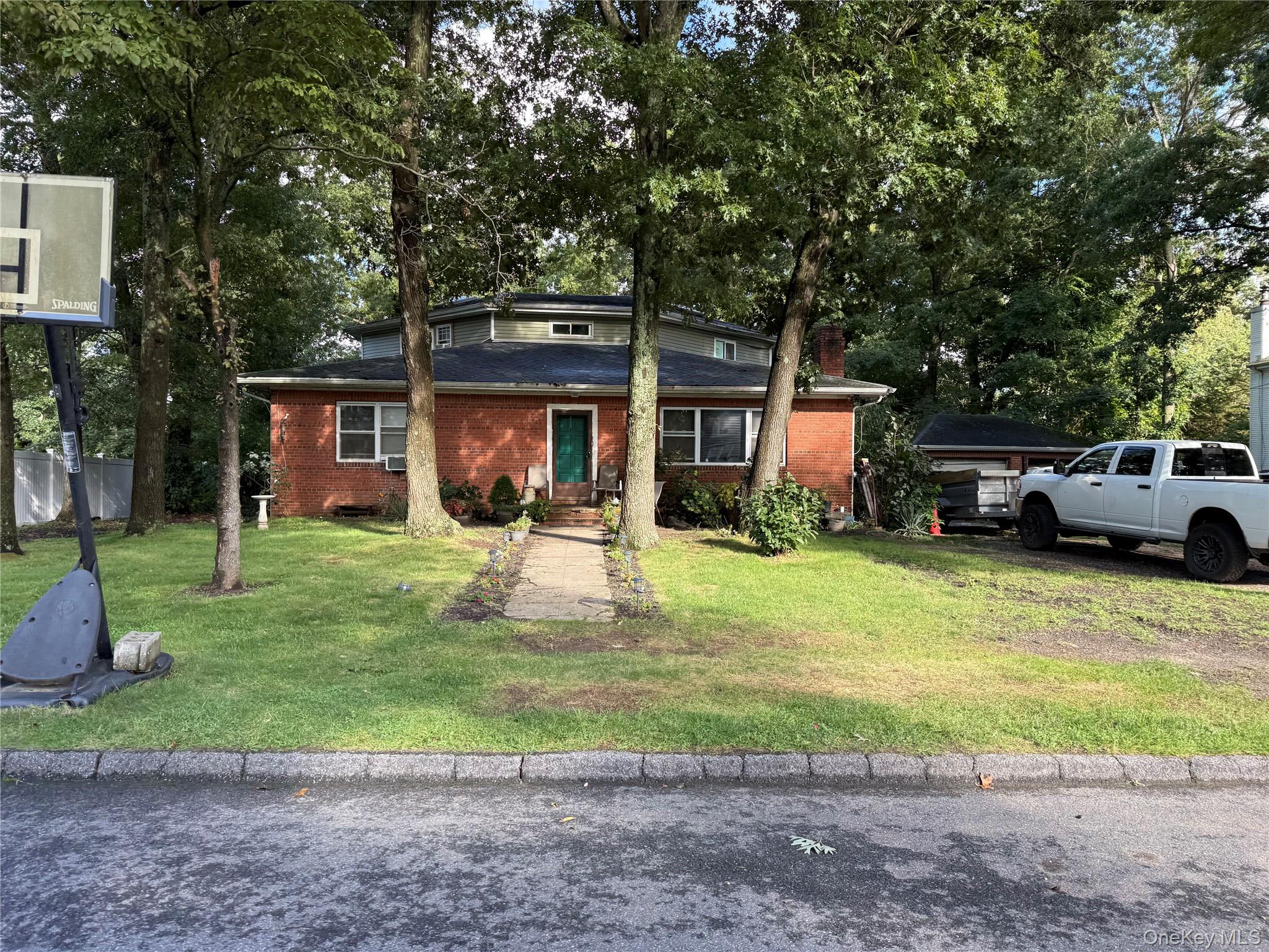 Brick-front house with a green entry door, mature trees, and a basketball hoop.