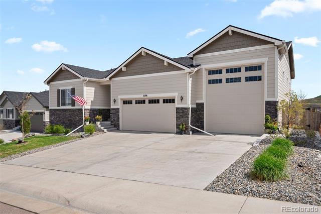 Beige two-story home with stone accents, a wide driveway, and a tall garage door.