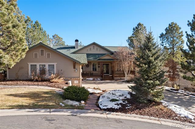 Tan single-story house with a covered porch, curved walkway, evergreen trees, and patches of snow.