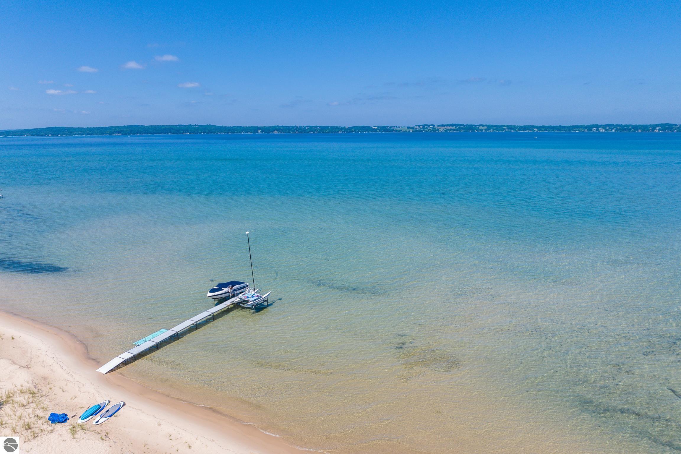 Sandy waterfront with a long dock, boats, and paddleboards on a calm lake.