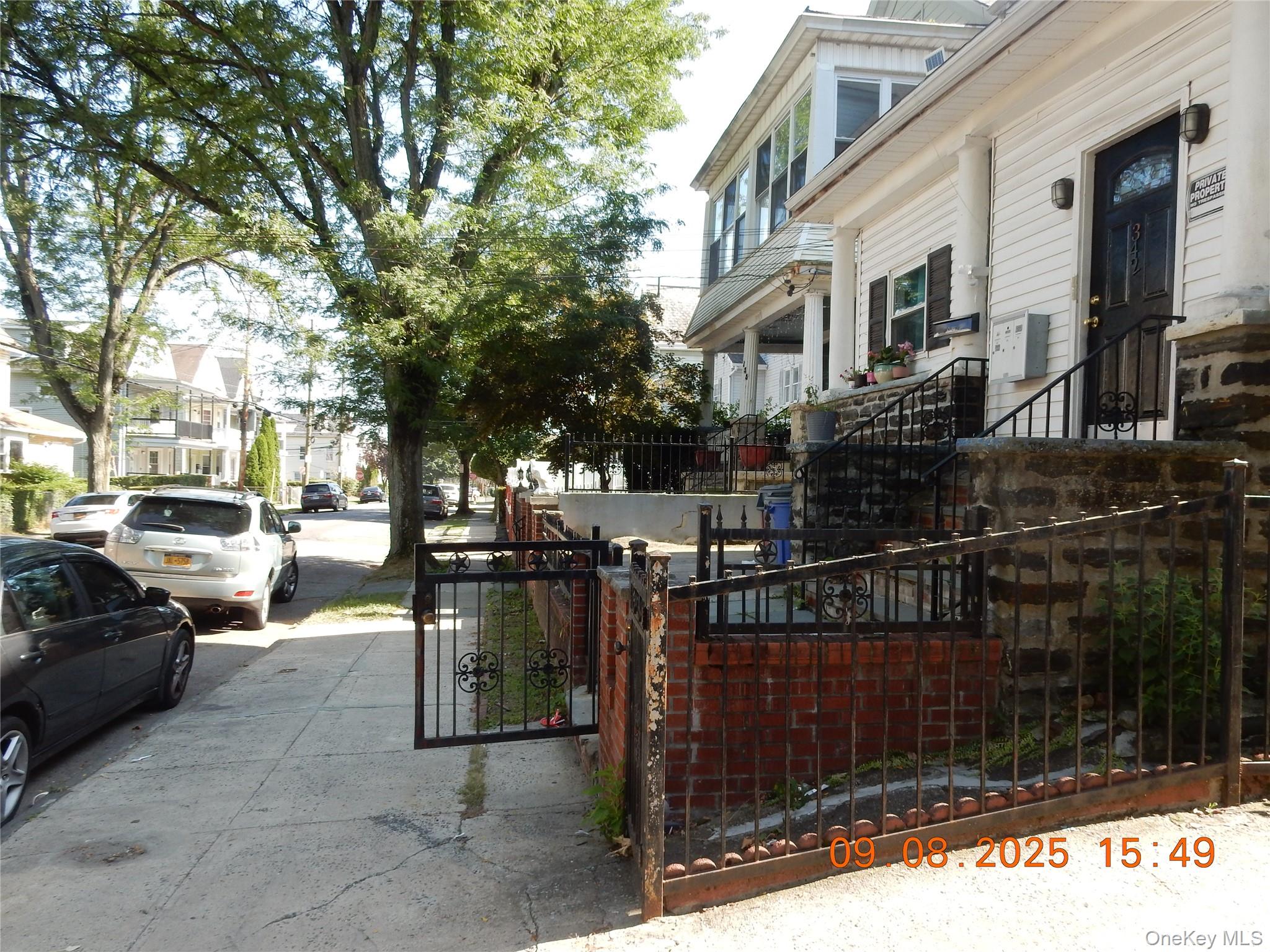 White-sided home with stone steps and black iron fencing beside a tree-lined residential sidewalk.