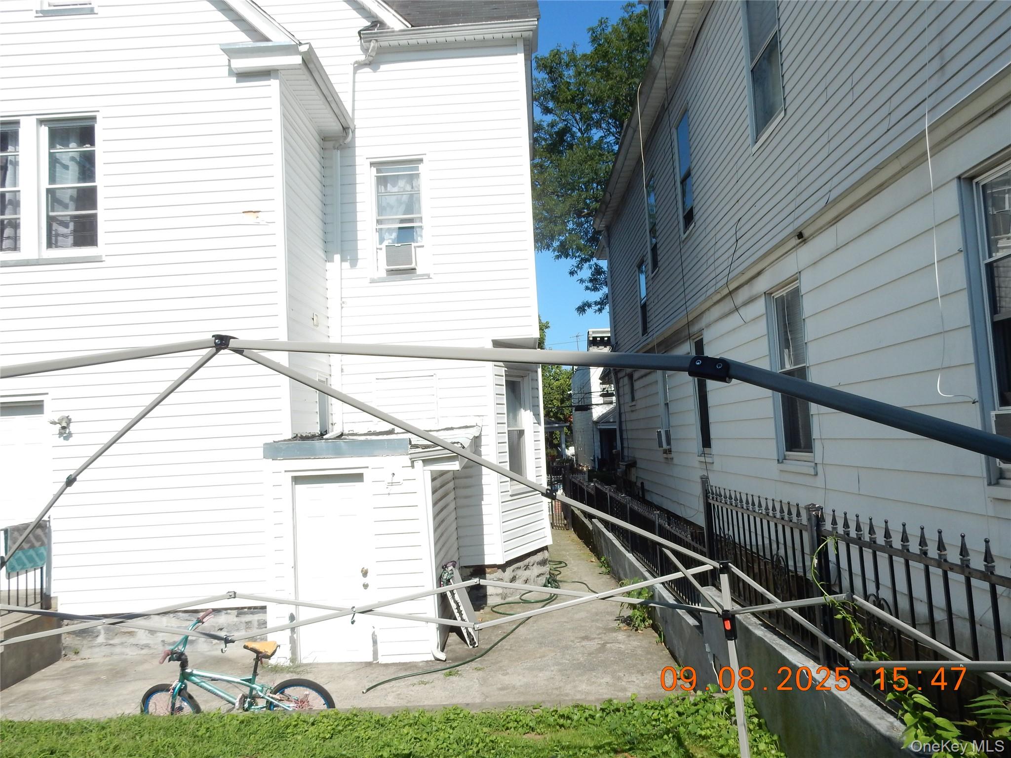 Narrow side yard between houses with a concrete walkway, metal fence, drying rack, and bicycle.