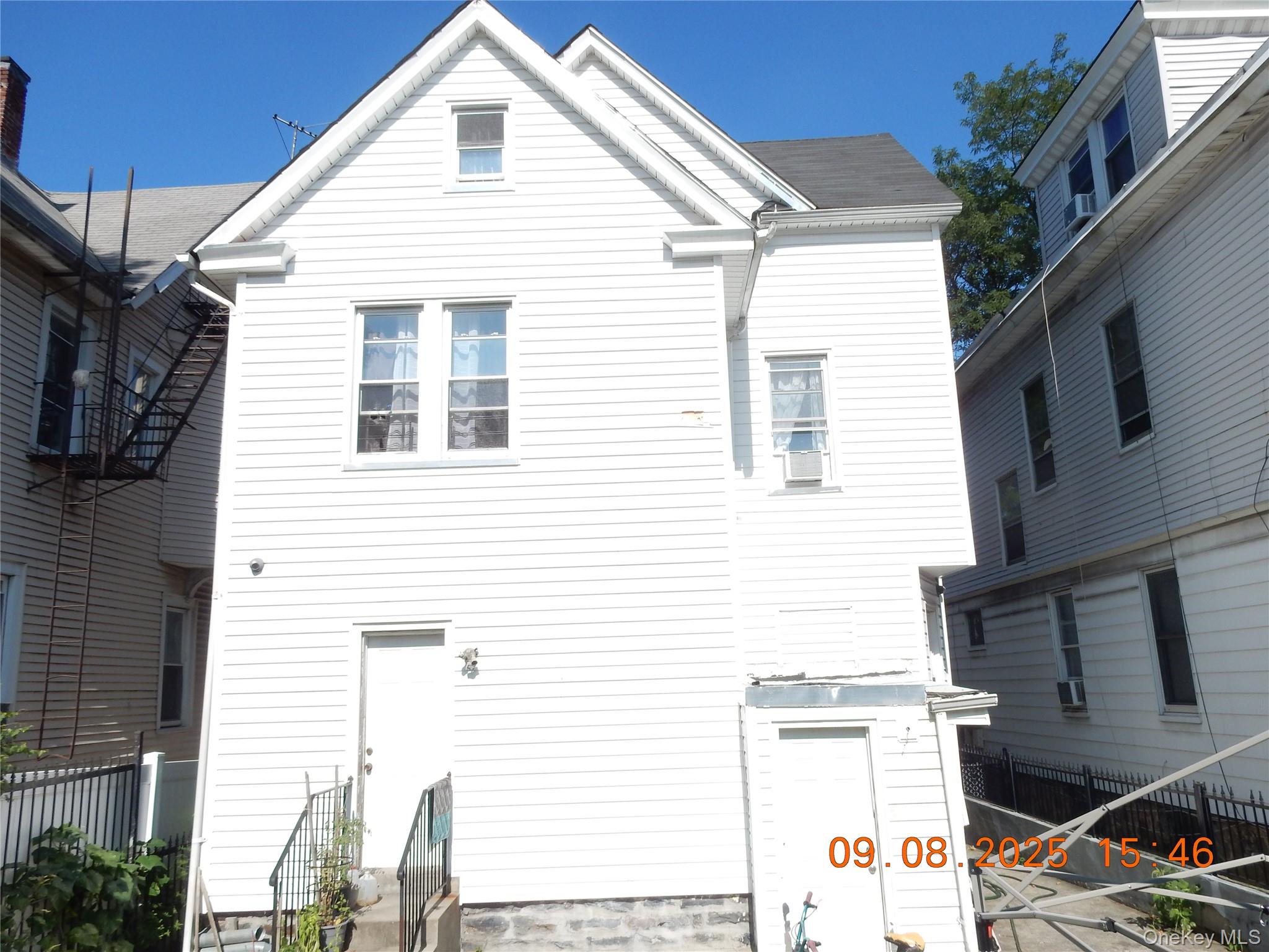 Rear of a white multi-story house with a steep gabled roof and neighboring homes close by.