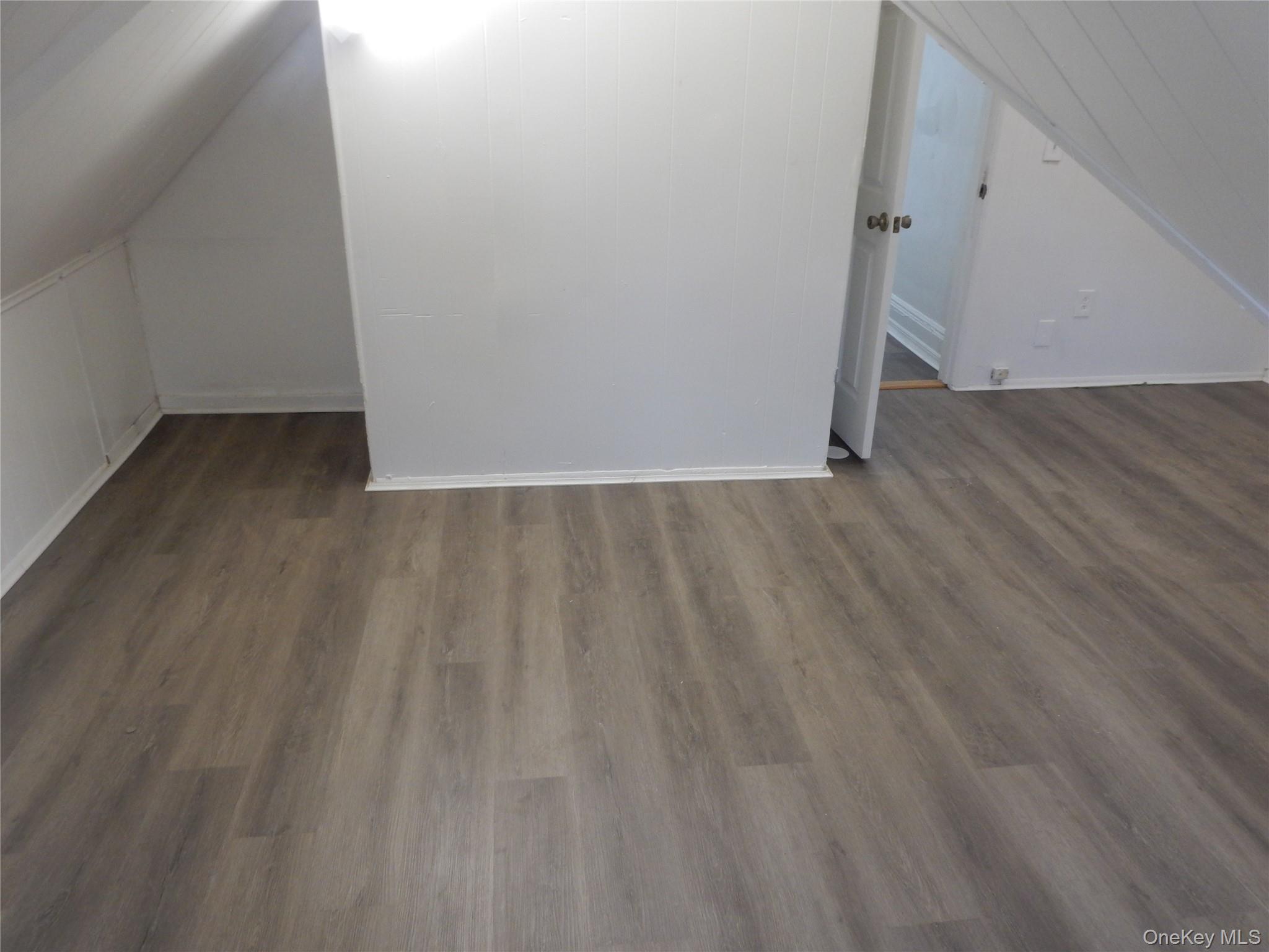 Vacant room with gray-brown plank flooring, sloped ceiling, and an open doorway.