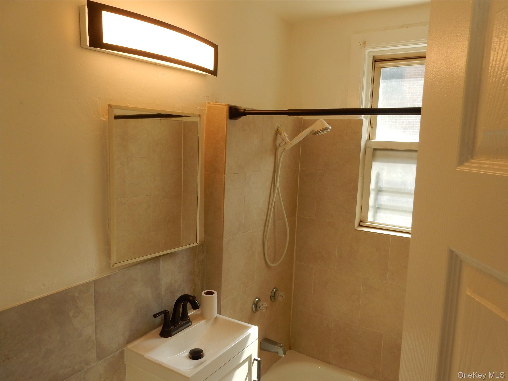 Bathroom with beige tile, a tub and handheld shower, and a small white vanity beneath a mirror.