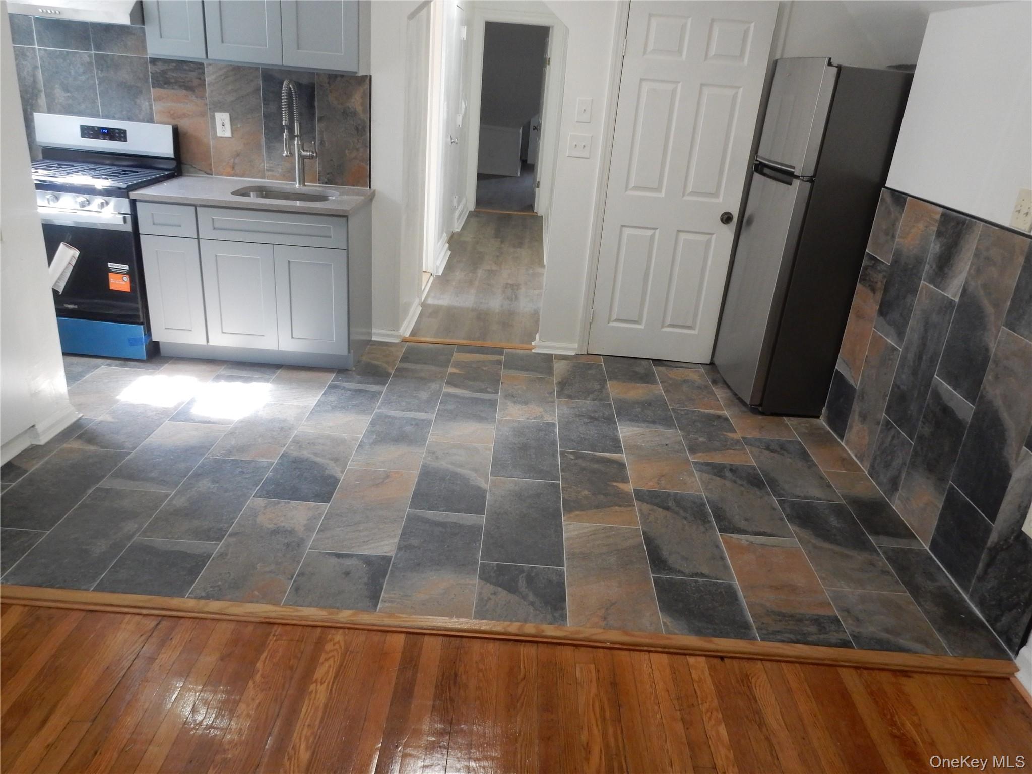 Kitchen with gray cabinets, stainless-steel appliances, and multicolored tile flooring and backsplash.