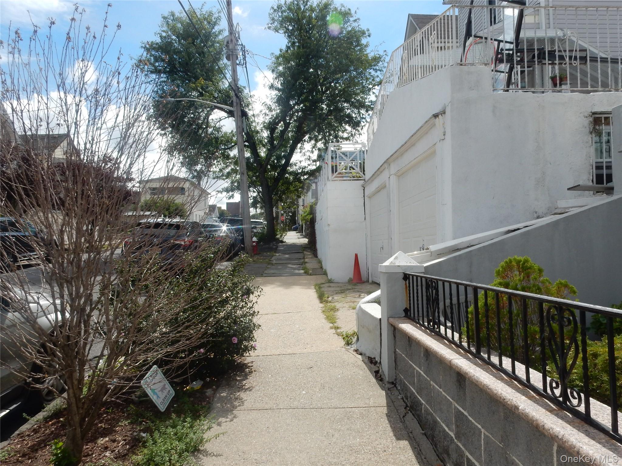 White building with garage doors and an elevated deck beside a tree-lined sidewalk.