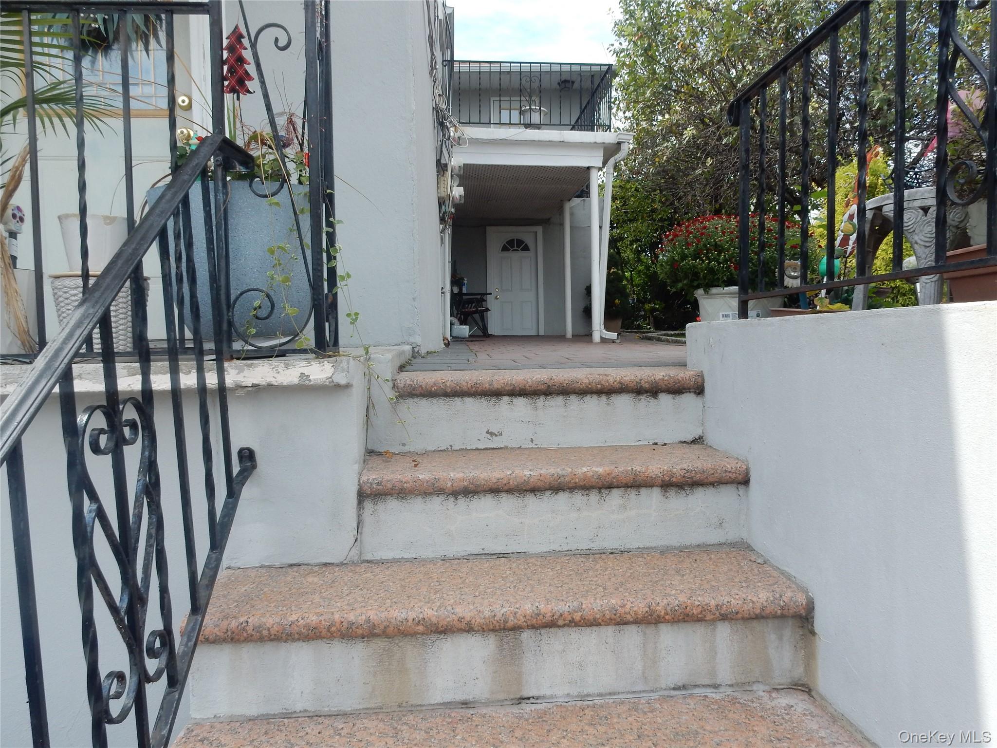 Stone steps with wrought-iron railings lead to a covered home entrance, framed by potted plants and greenery.