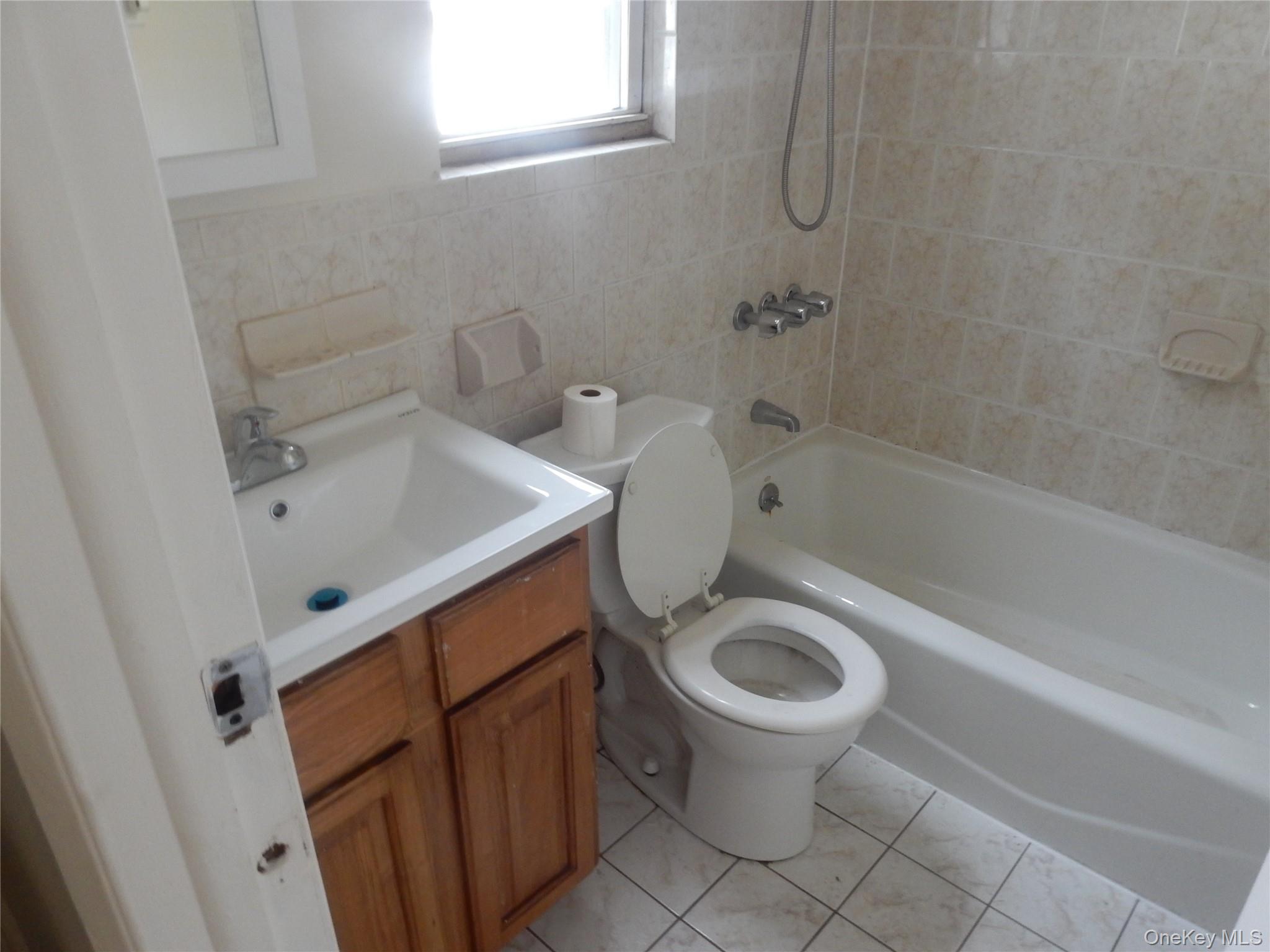 Bathroom with a wood vanity, white sink, toilet, and tiled bathtub with handheld shower.