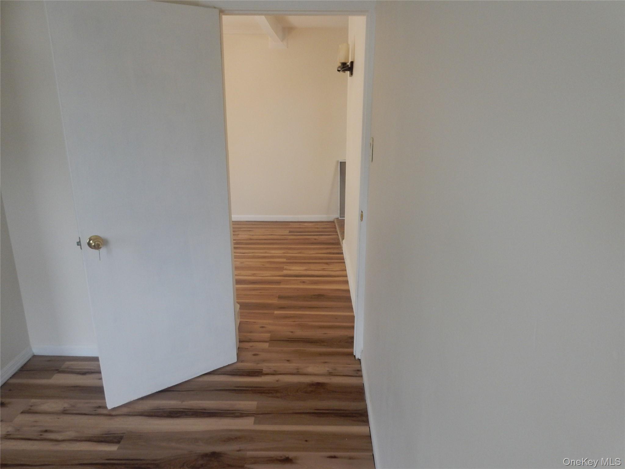 Vacant interior with an open white door, wood plank floors, and a wall sconce.