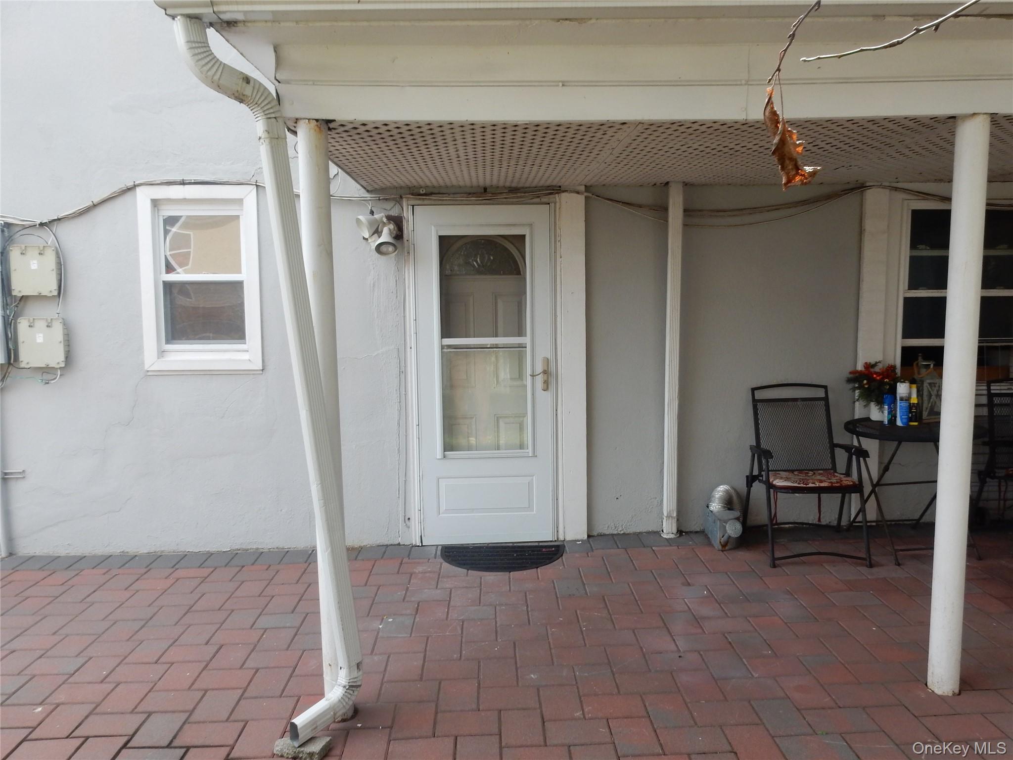 Covered front porch with a white entry door, brick pavers, and a small seating area.
