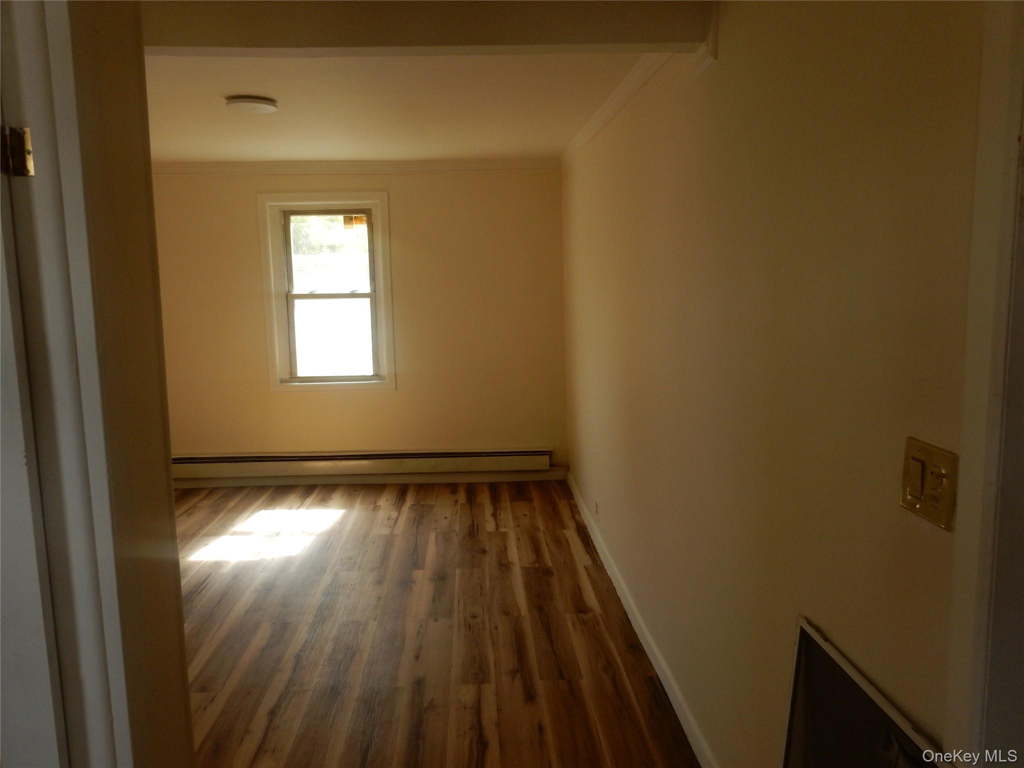 Vacant room with wood flooring, a single window, and a baseboard heater.