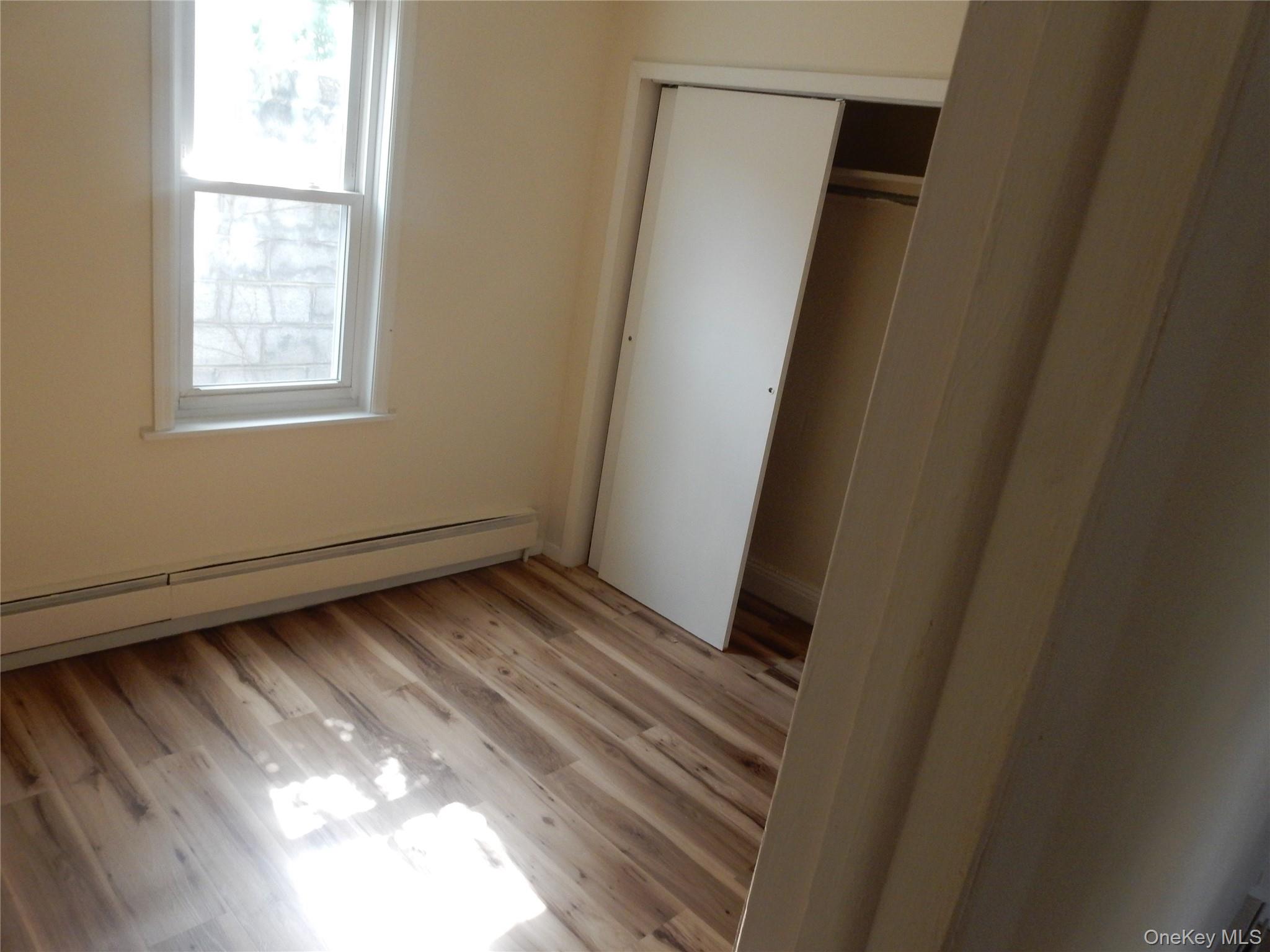 Empty bedroom with wood flooring, a window, and a partially open closet.