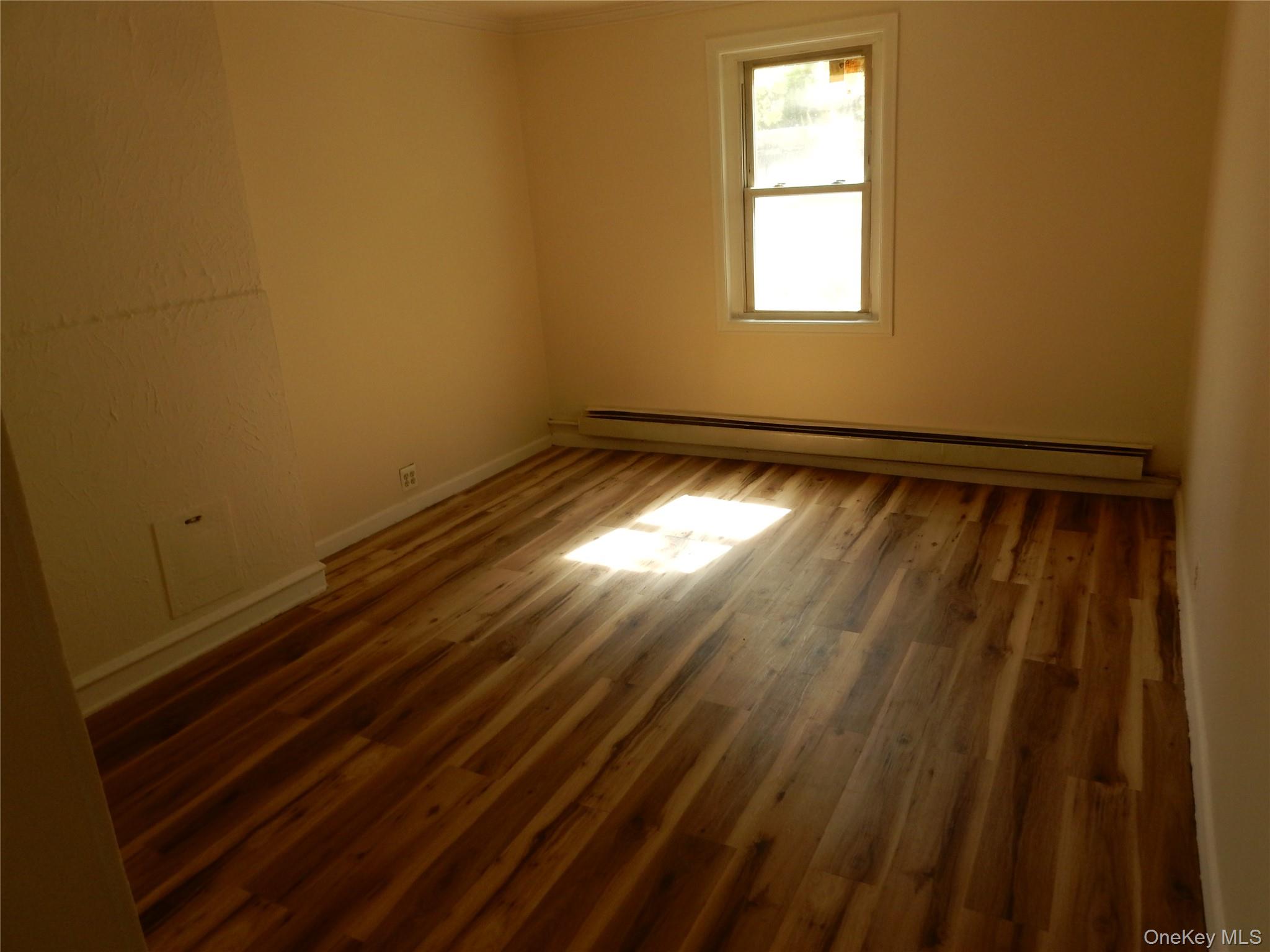Empty room with hardwood floors, a single window, and a baseboard heater.