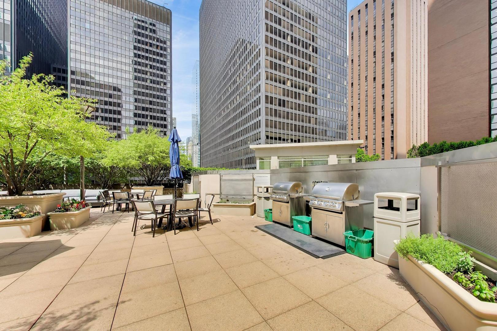 Rooftop terrace with dining tables, barbecue grills, and planters among downtown high-rises.