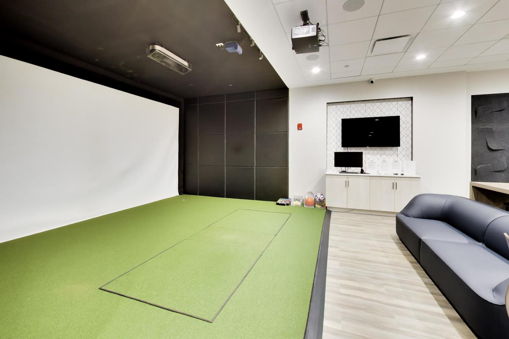 Amenity room with a large projection screen, green putting surface, and curved dark sofa.