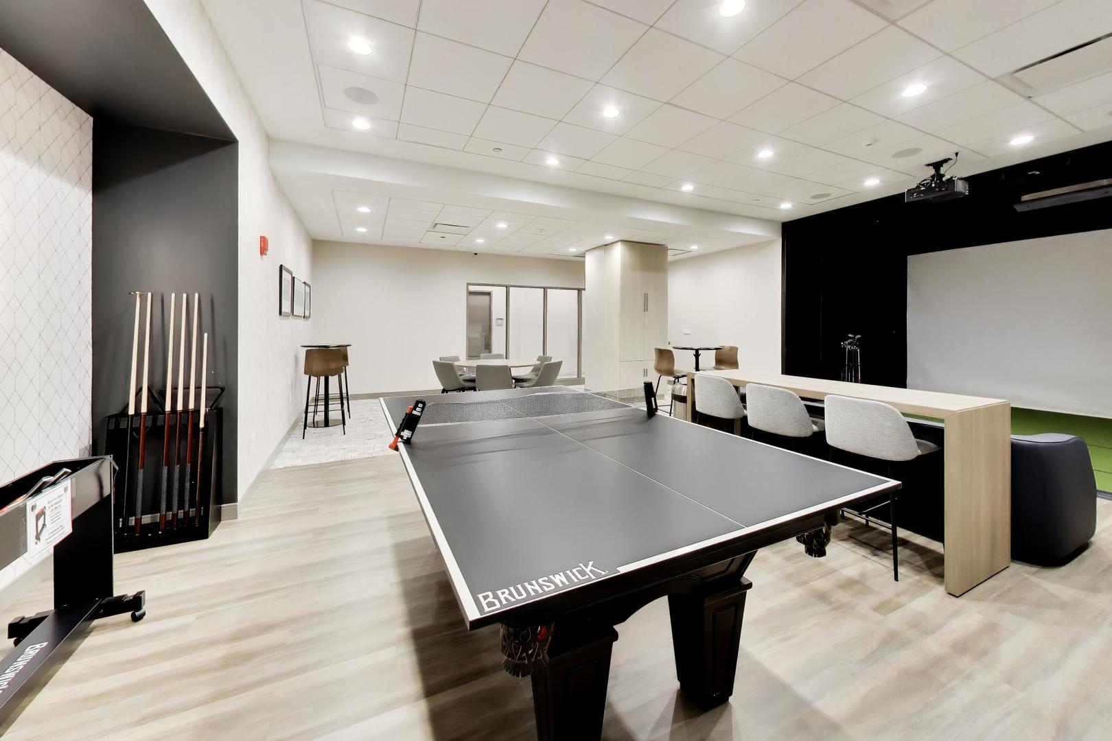 Building recreation room with a table tennis table, lounge seating, and a large projection screen.