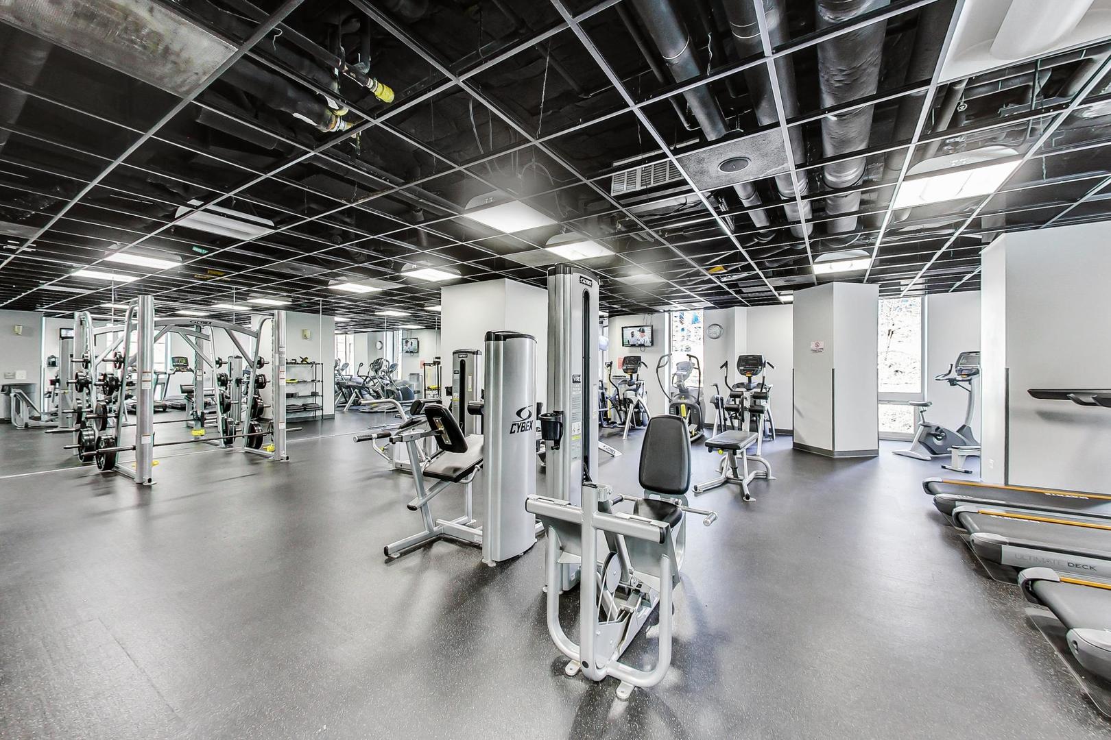 Condominium gym with weight machines, cardio equipment, and windows.