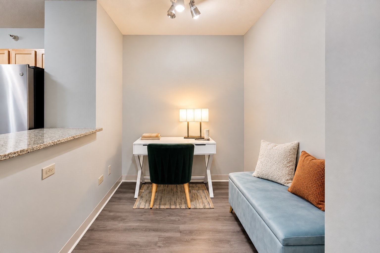 Condo work nook with a white desk, dark green chair, and light blue sofa.
