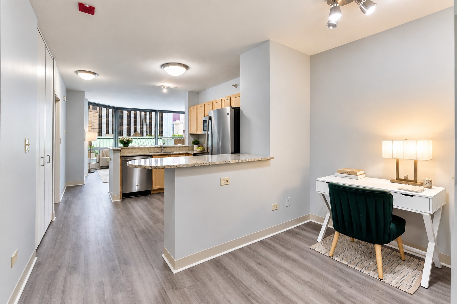Condo kitchen with granite breakfast bar and stainless appliances beside a desk overlooking city buildings.