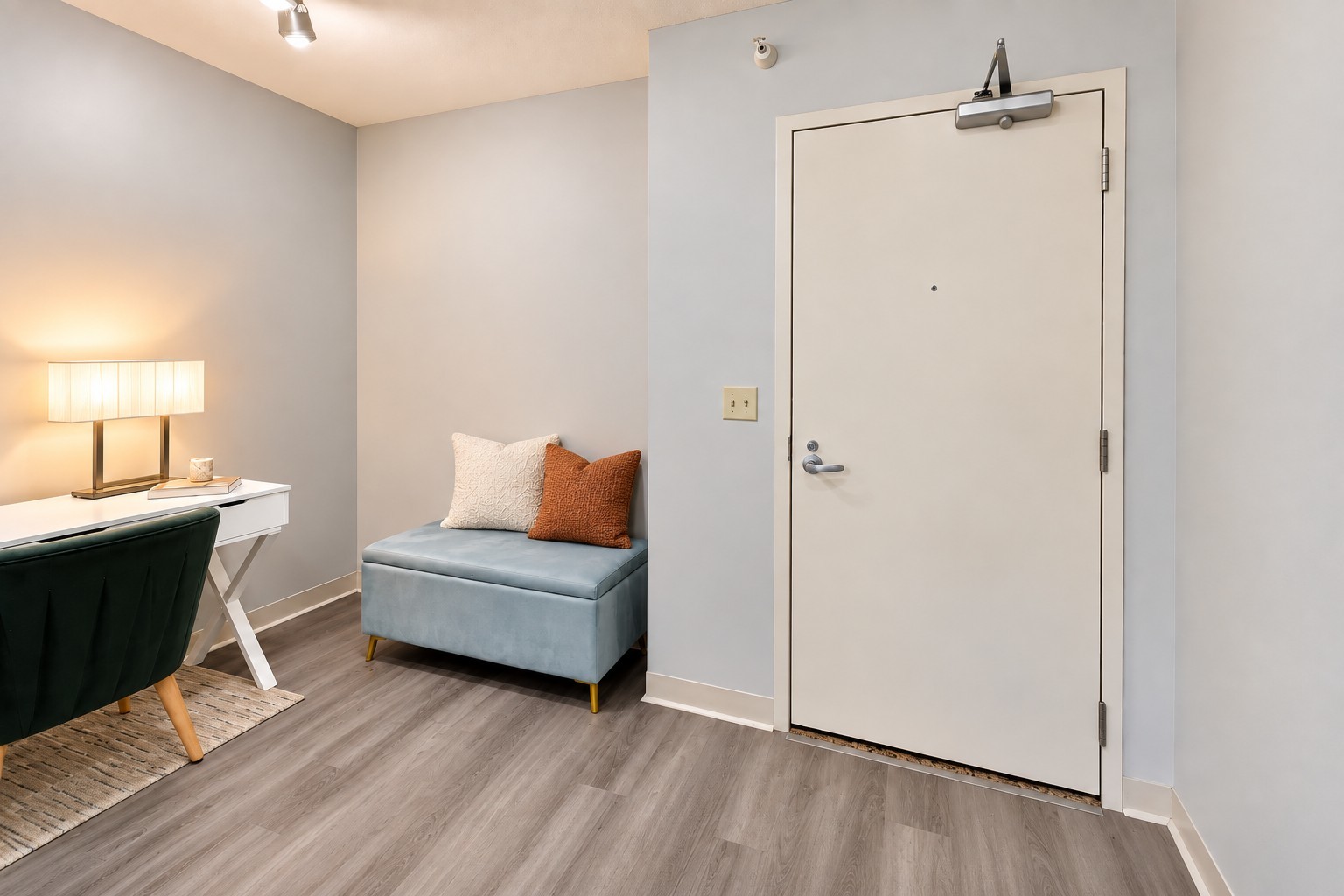 Condo entryway with a white front door, upholstered bench, and desk with a green chair.