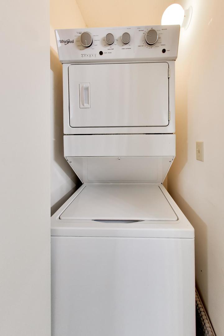 Stacked Whirlpool washer and dryer in a narrow laundry closet, with a top-loading washer.
