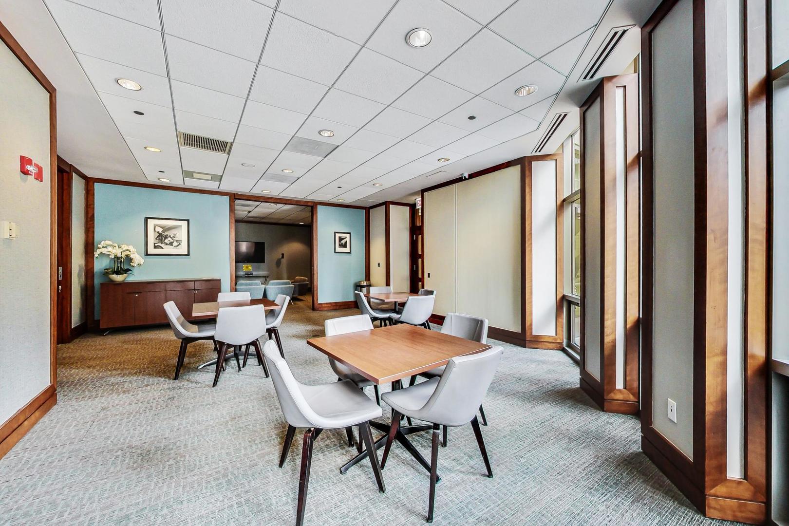 Furnished meeting room with wooden tables, white chairs, blue walls, and large windows.