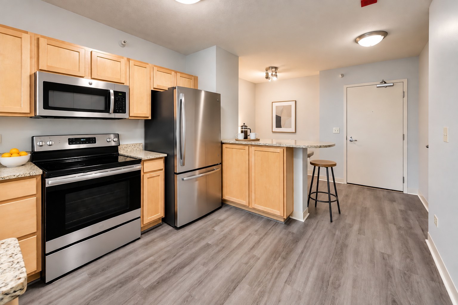 Condo kitchen with maple cabinets, stainless steel appliances, and a breakfast bar with a stool.
