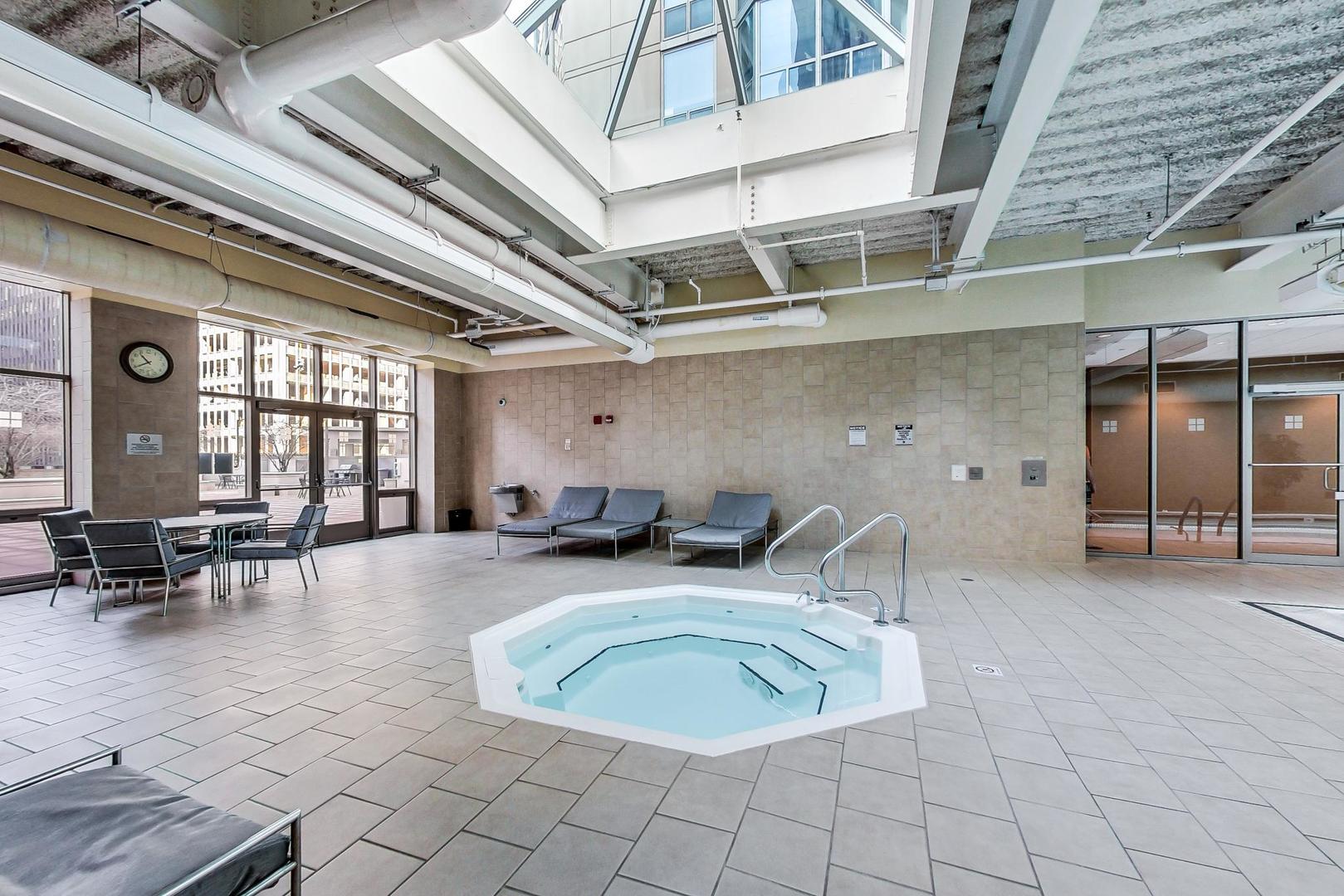 Indoor pool and hot tub with lounge seating beside large windows.