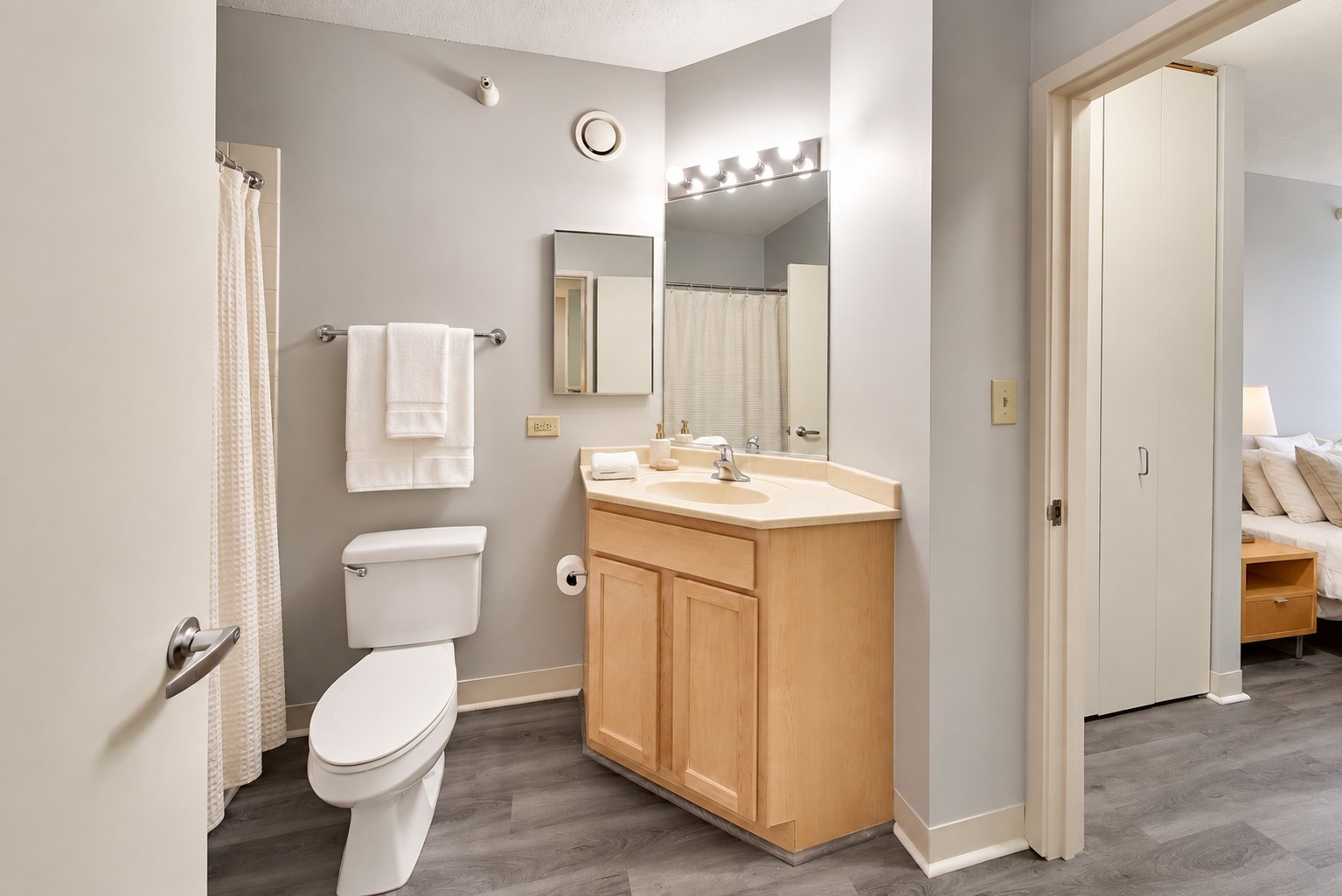 Bathroom with a light wood vanity, illuminated mirror, and white shower curtain.