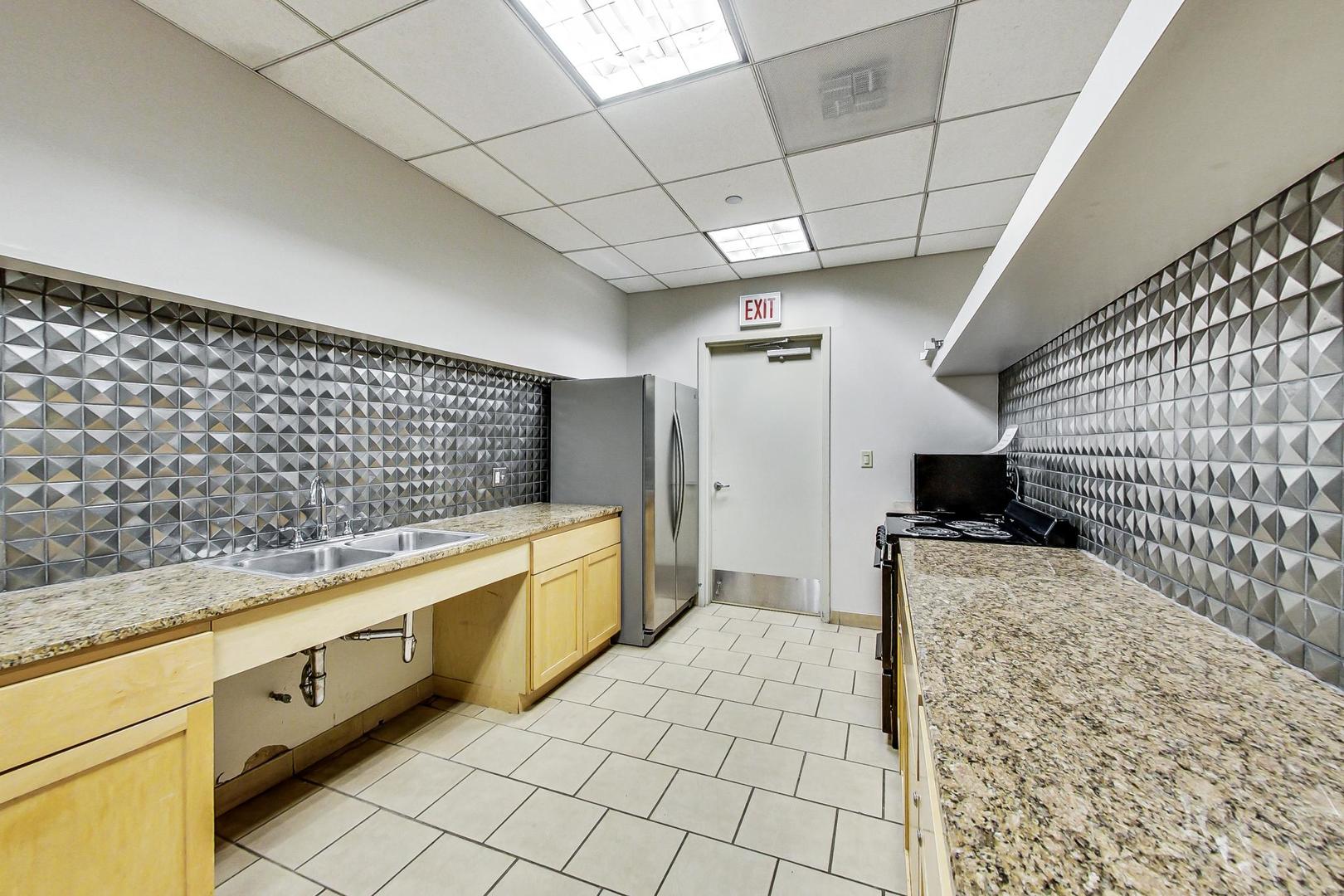 Kitchen with granite counters, light wood cabinets, stainless steel appliances, and geometric metallic backsplash.
