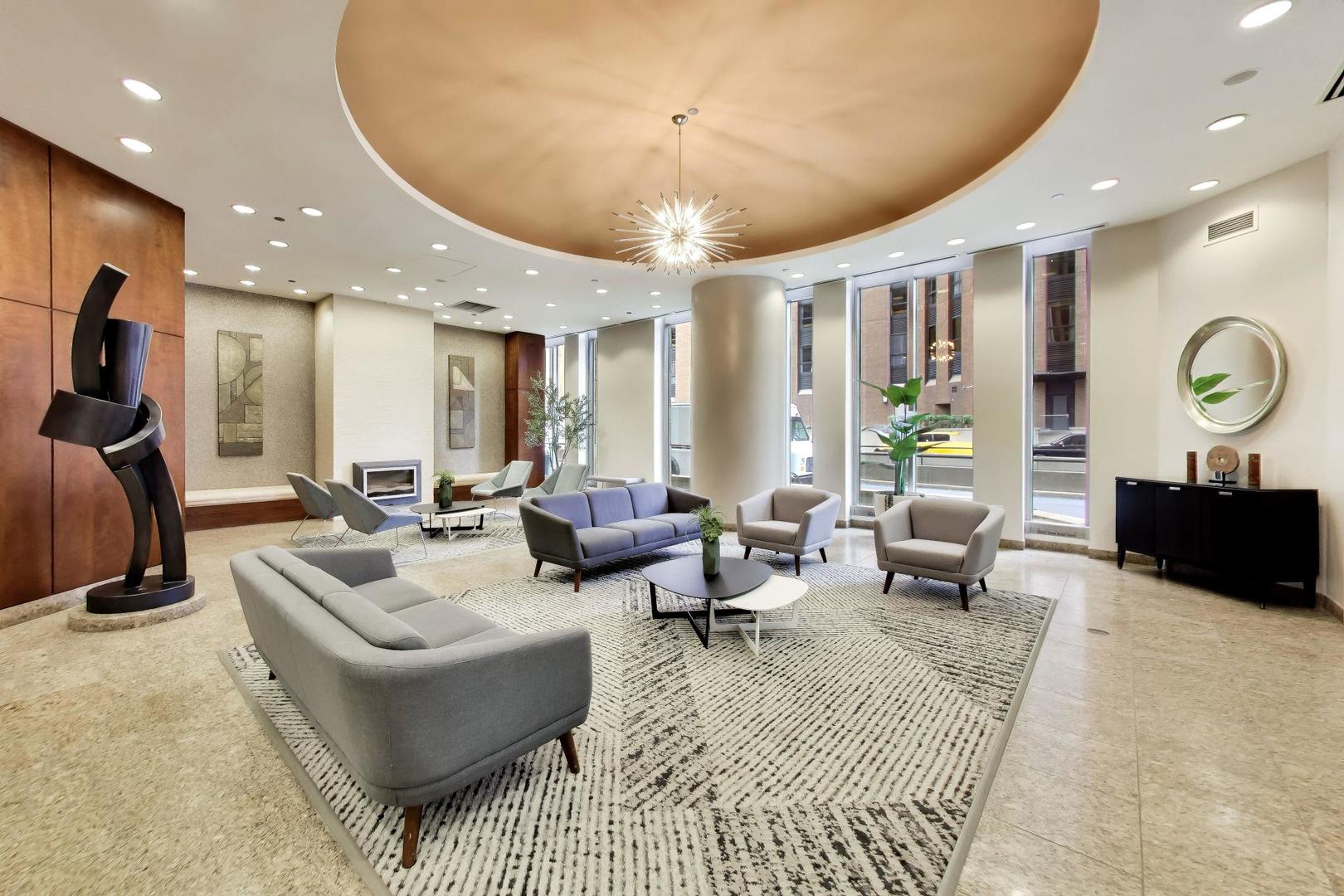 Furnished condo lobby lounge with gray seating, a modern sculpture, and a starburst chandelier.