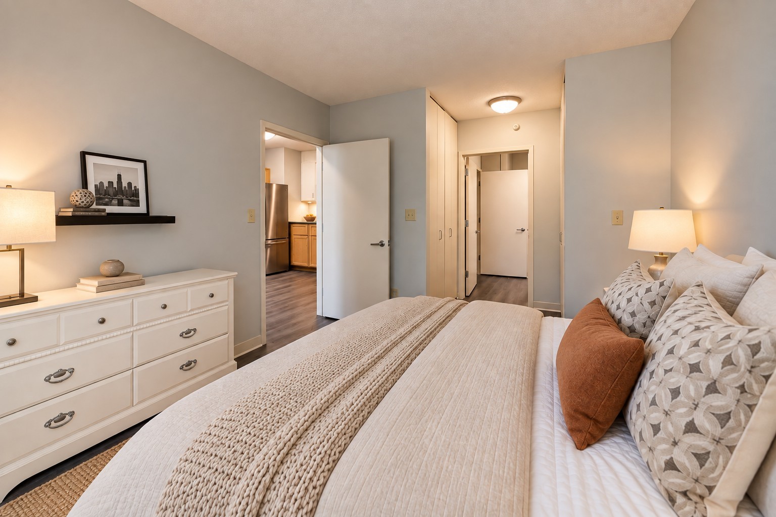 Furnished bedroom with a large bed, white dresser, and built-in closets.