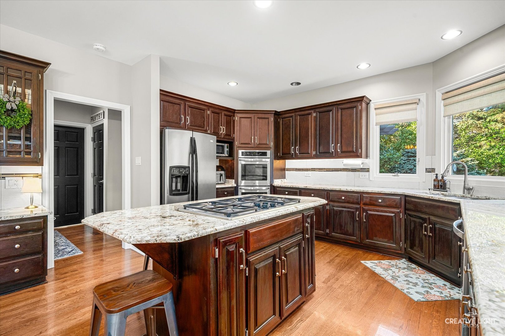 Kitchen with dark wood cabinetry, a granite island and gas cooktop, stainless steel appliances, and hardwood floors.