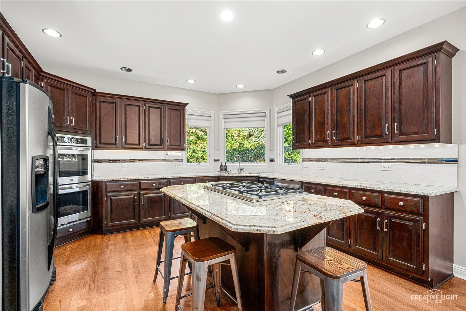 Kitchen with dark wood cabinets, granite island with gas cooktop, and stainless steel appliances.