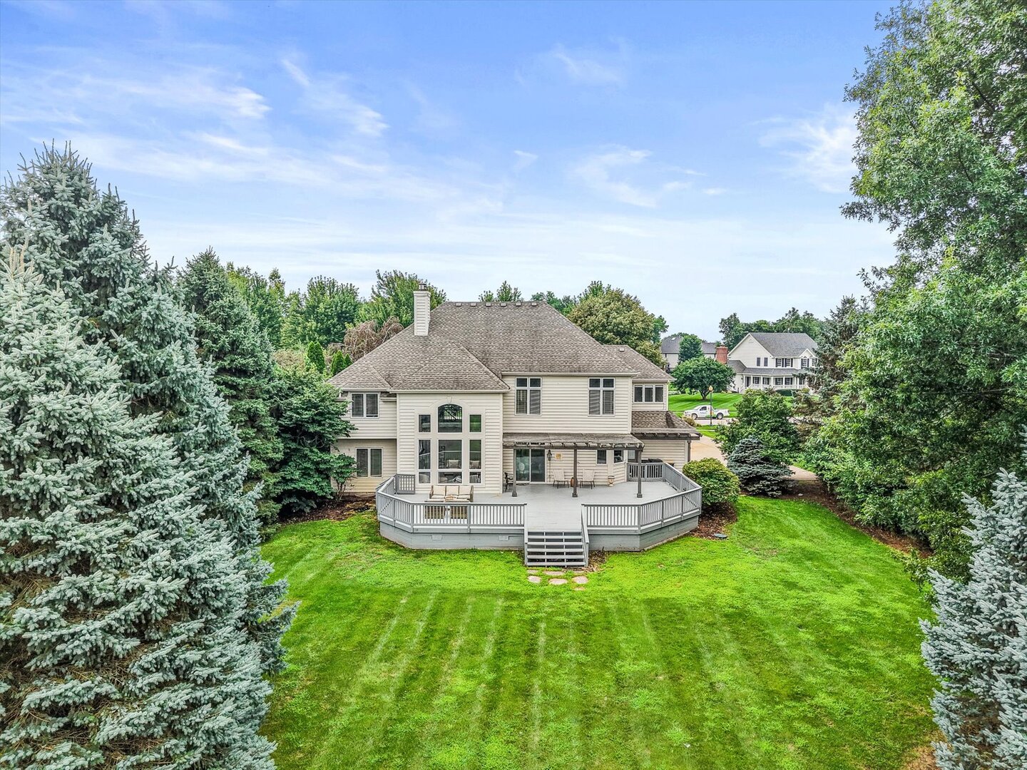 Rear of a large home with a broad deck and stairs overlooking a tree-lined lawn.
