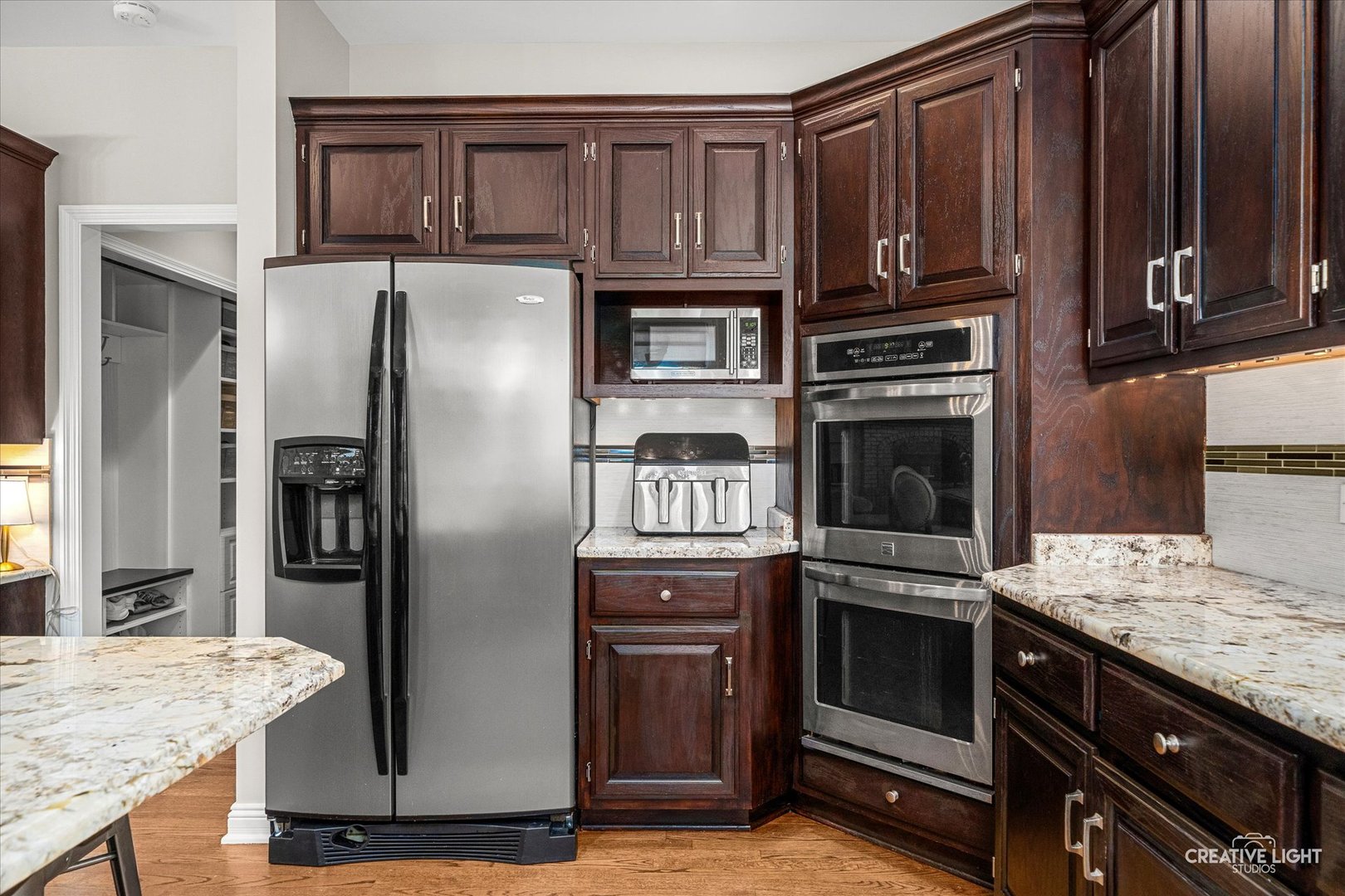 Kitchen with dark wood cabinets, granite counters, stainless refrigerator, and double wall ovens.