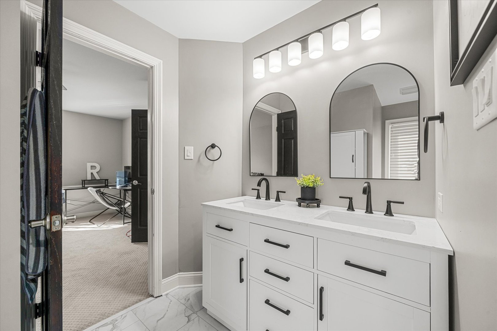 Bathroom with a white double vanity, black fixtures, and two arched mirrors.