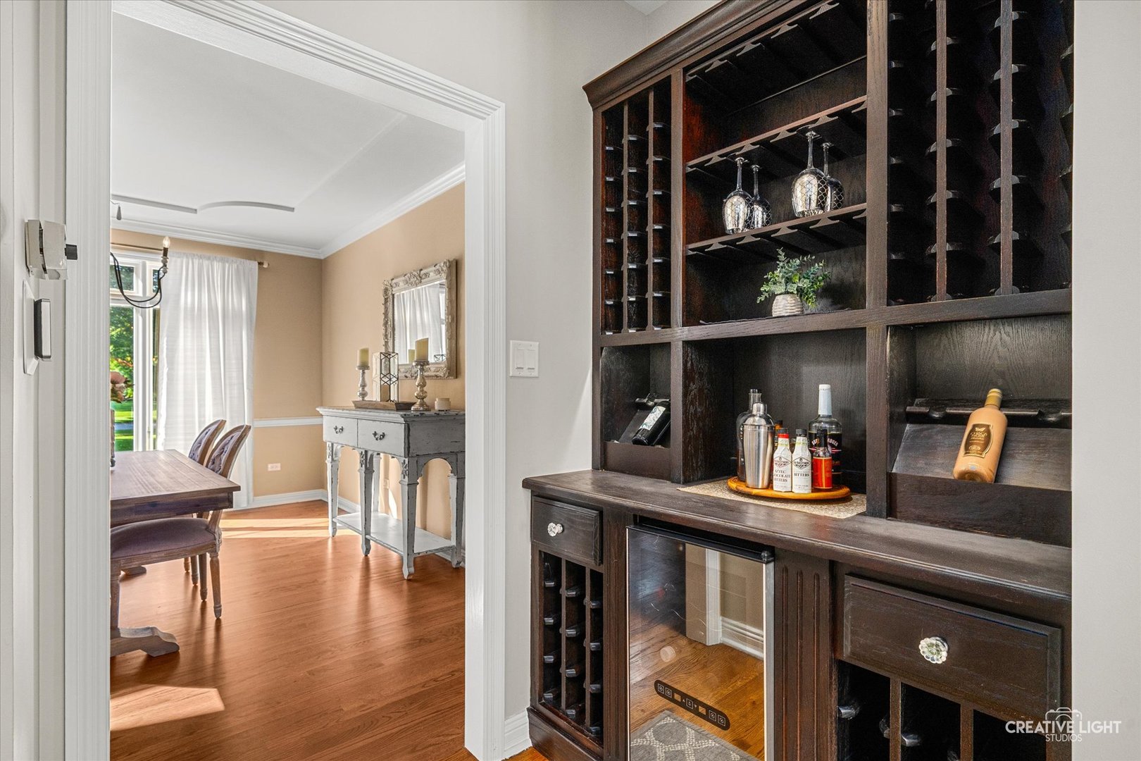 Built-in dark wood wine bar with wine racks and beverage refrigerator beside a dining room.